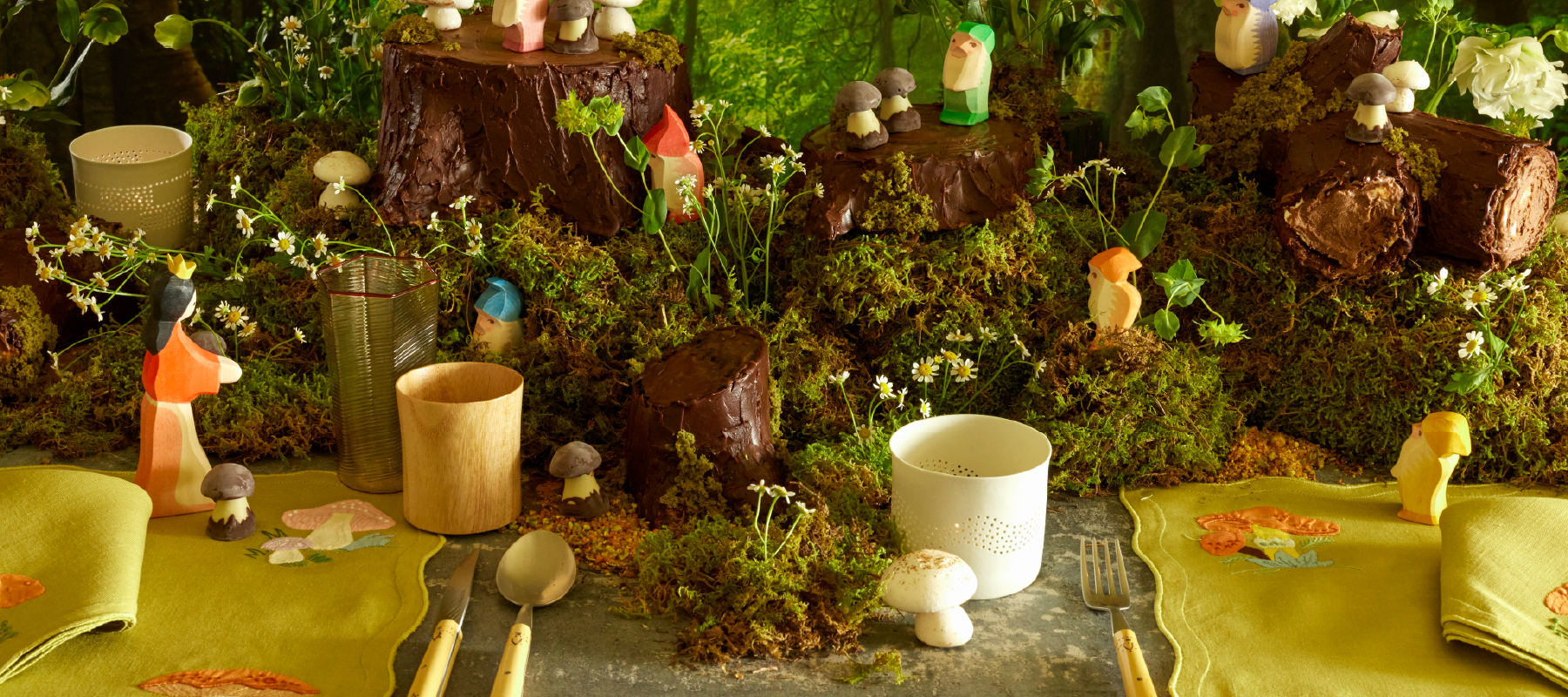 Magical forest table setting with mushroom applique napkins and placemats, wooden figurines, and a forest-themed cake.