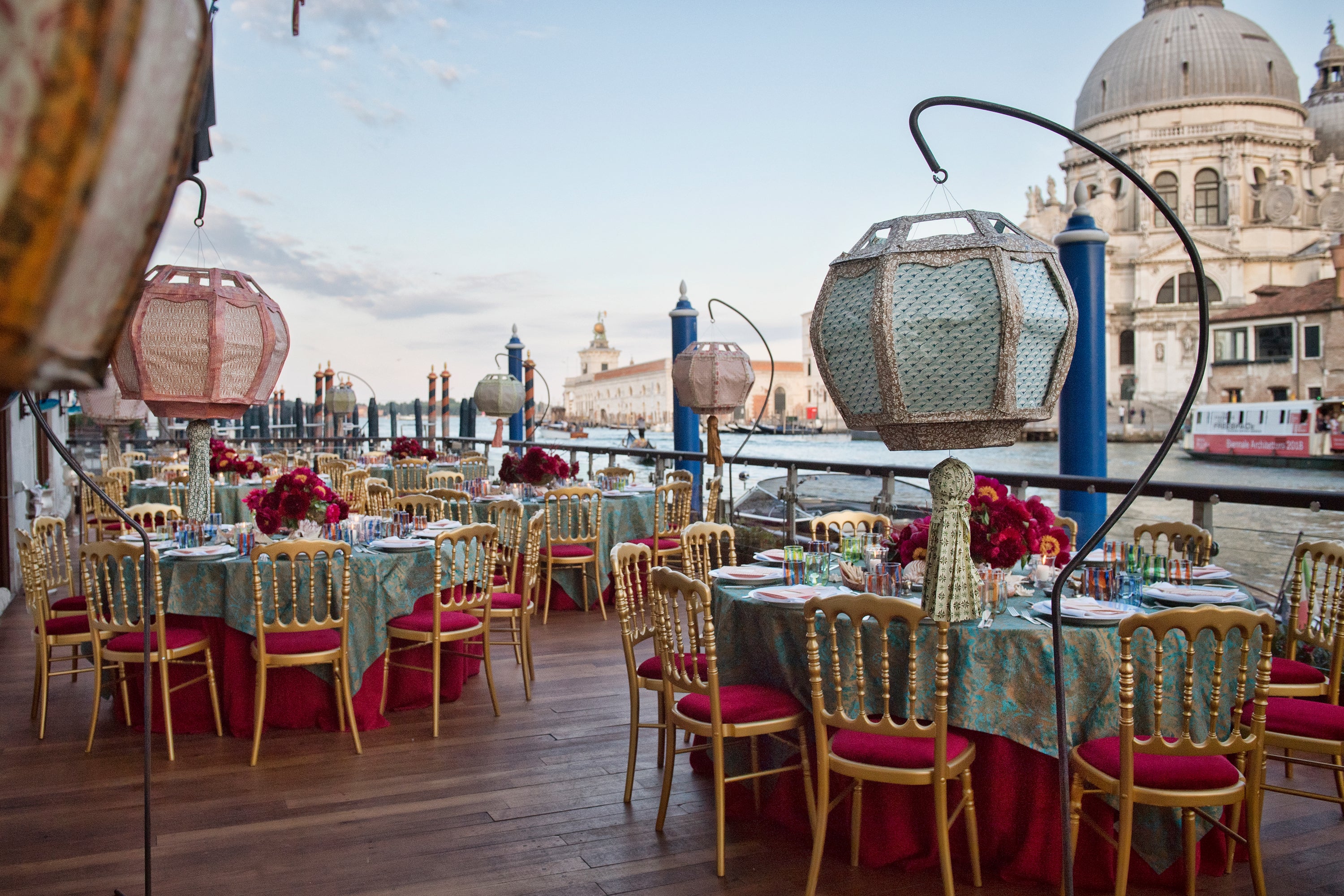 Luxurious private celebration near a canal with colorful tablecloths, unique environmental installations, and oversized lighting in Venice, Italy.