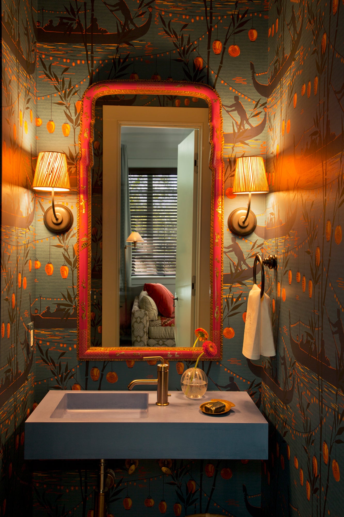 Bold powder room transformation featuring hand-painted chinoiserie wallpaper in teal with copper accents, framed by a coral-trimmed mirror and brass sconces – exemplifying Houses & Parties' fearless approach to small spaces through rich color, pattern, and unexpected details that create jewel-box moments within the home.