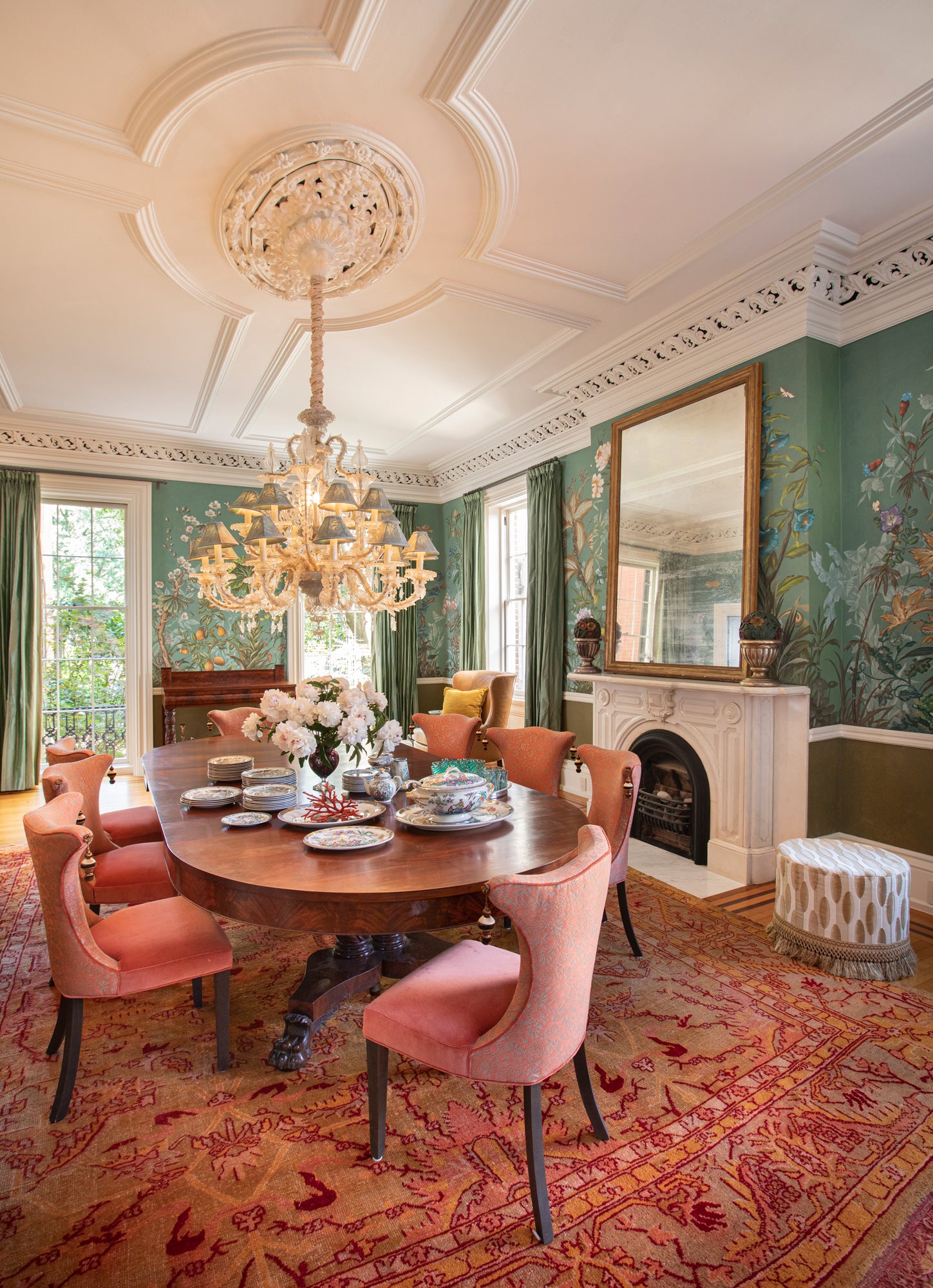 Stunning formal dining room featuring hand-painted chinoiserie wallpaper in celadon green, antique pedestal table surrounded by coral upholstered chairs, dramatic Murano glass chandelier, and classical architectural details – exemplifying Houses & Parties' masterful integration of color, pattern, and historical references to create elegant dining spaces that balance formality with warmth.