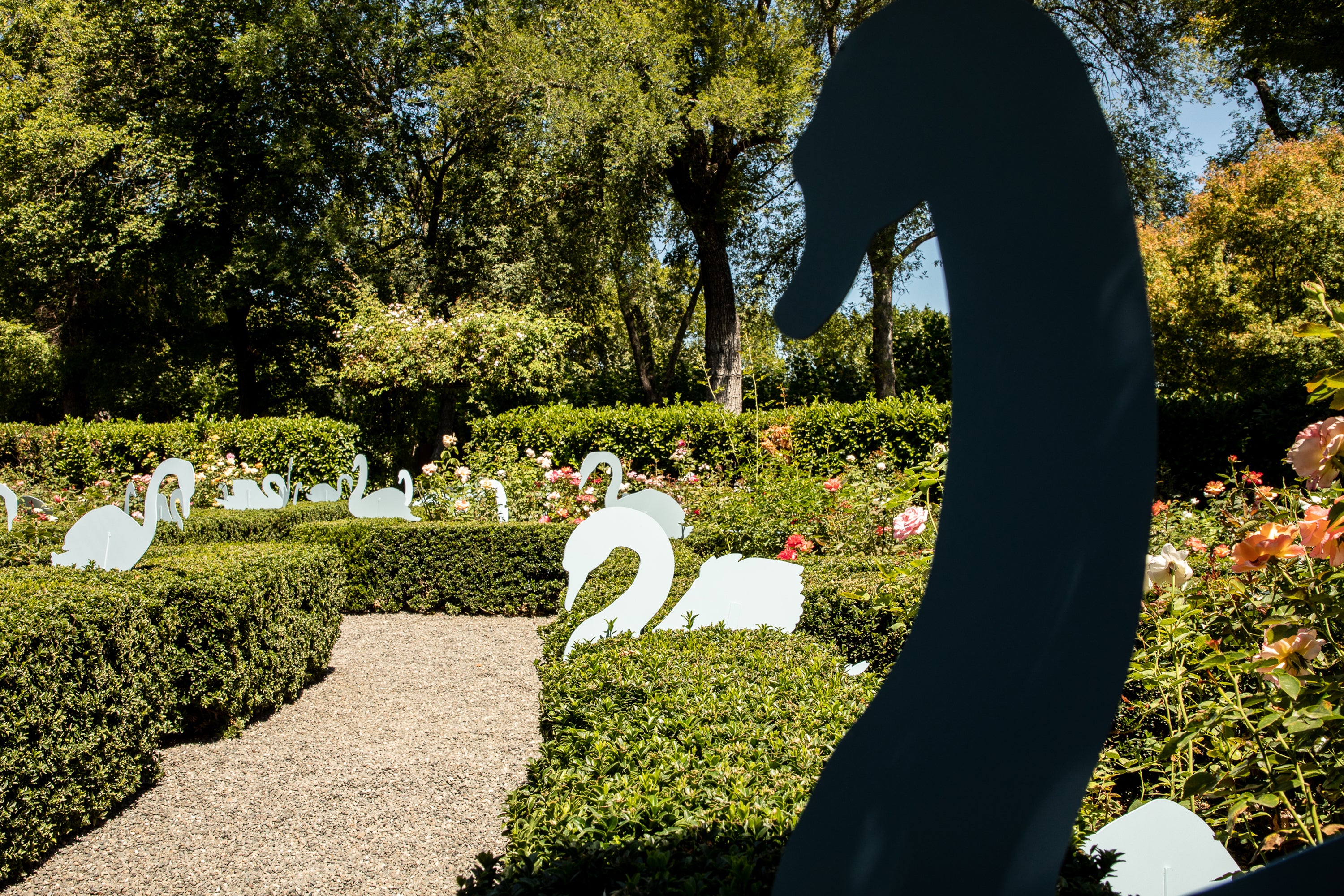 Whimsical garden installation for wedding featuring elegant white swan silhouettes nestled among manicured hedges and blooming roses.