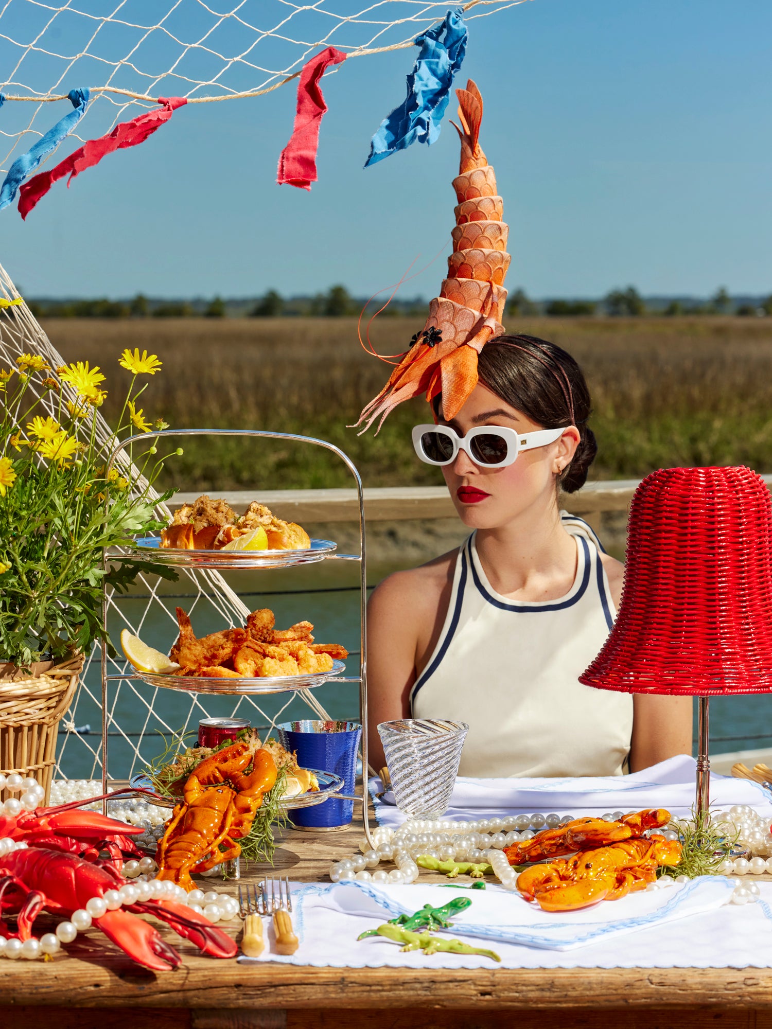 Summer tablescape with wicker lampshade, wicker basket, ceramic lobsters, and silver tea stand.