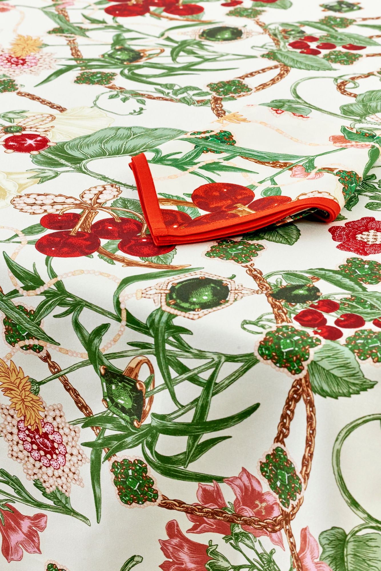 Floral tablecloth with red flowers and green leaves on a white background.