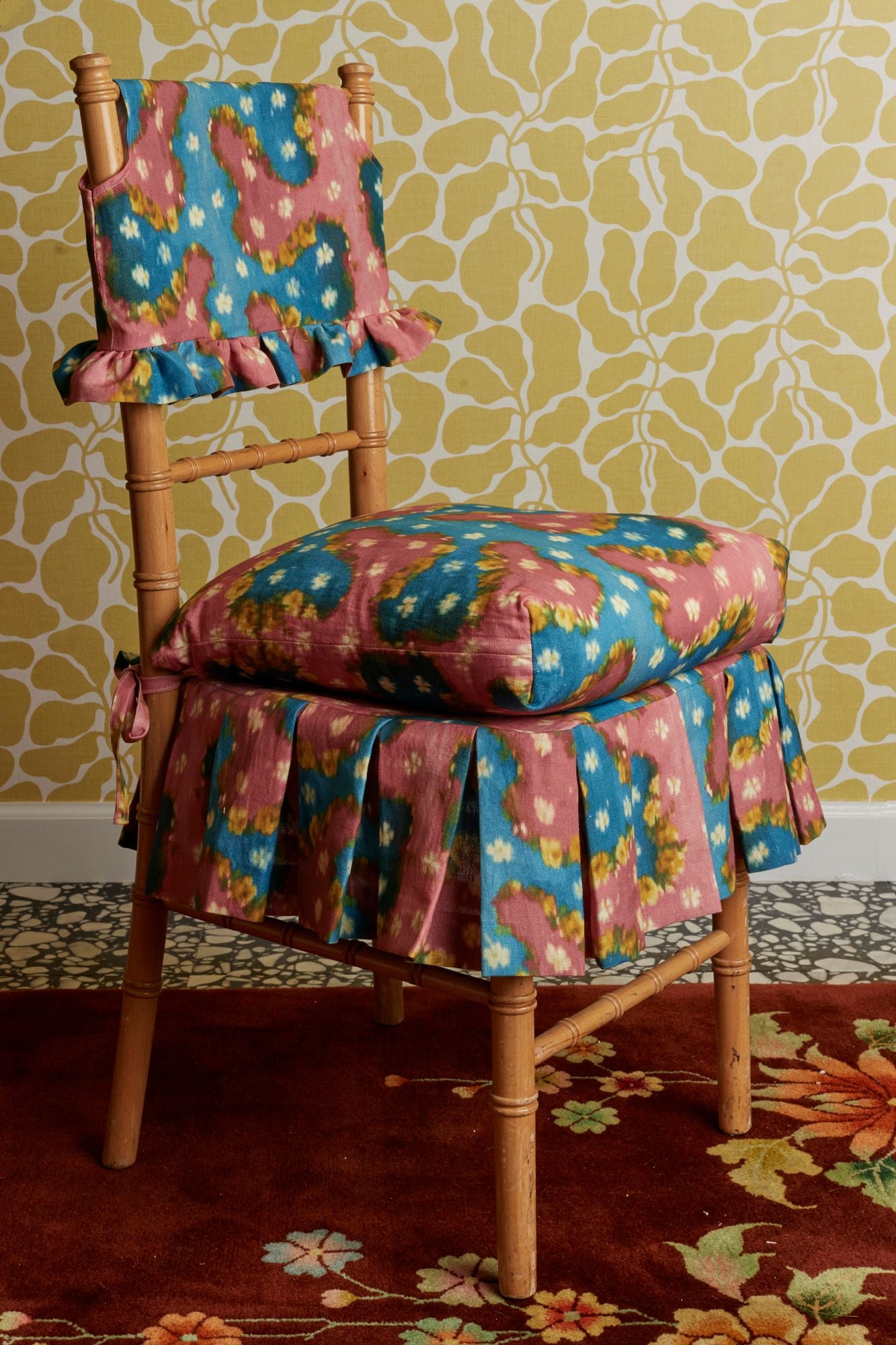Chair with colorful floral cushion against a patterned wall.