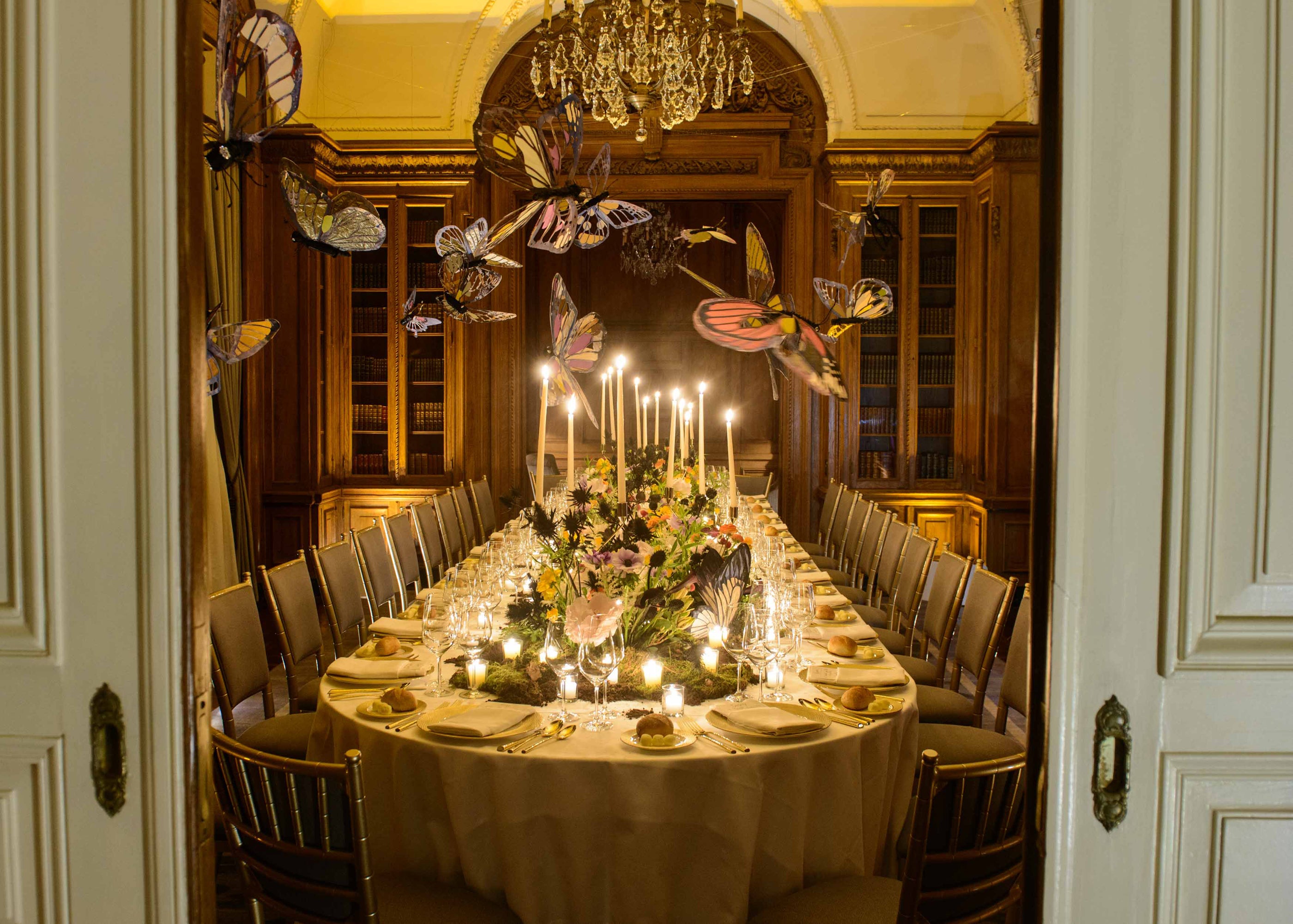 A beautifully set dining table with candles and flowers, surrounded by decorative butterflies, in an elegant room.