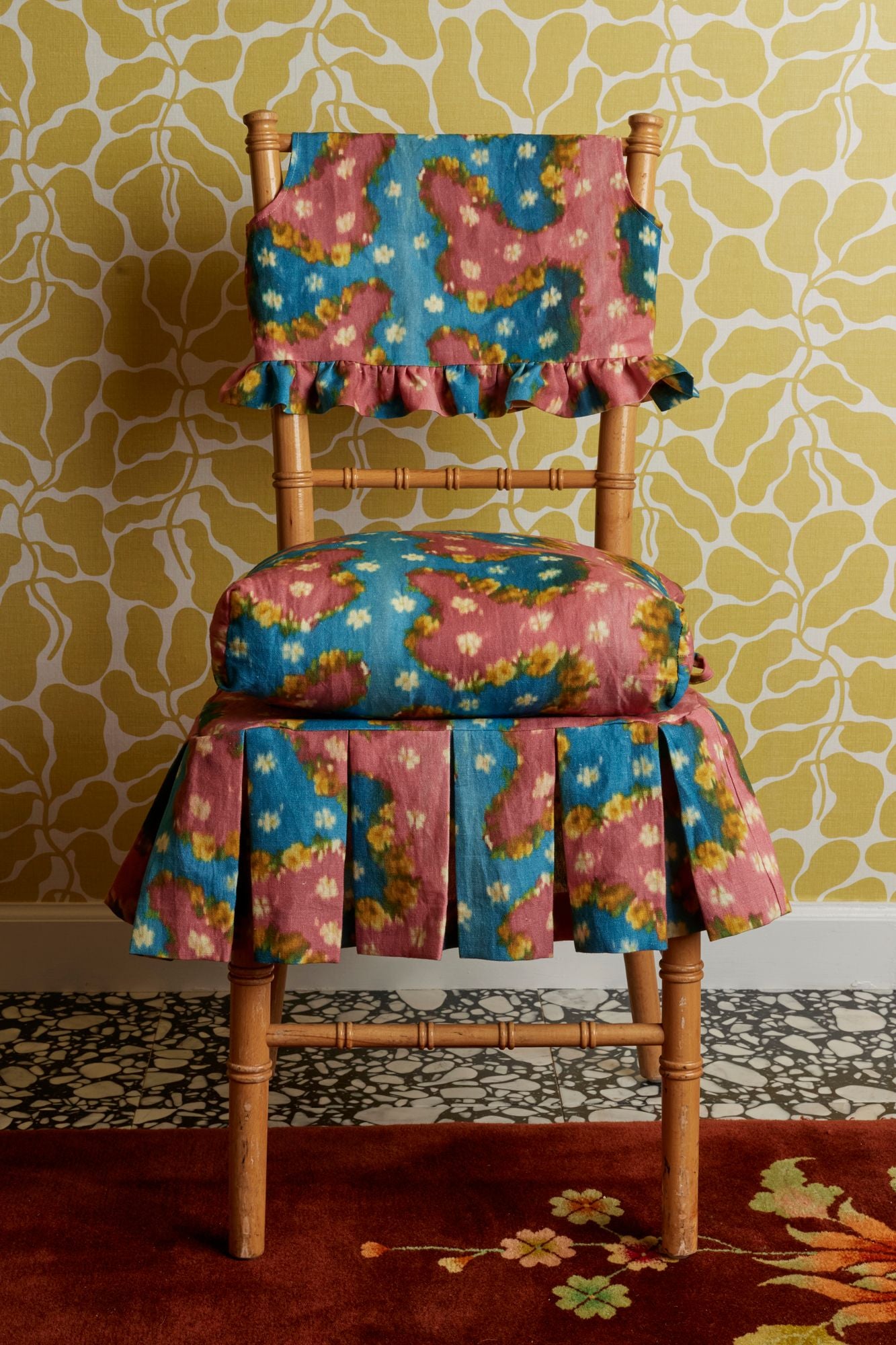 Chair with colorful floral patterned cover against a yellow patterned wall.