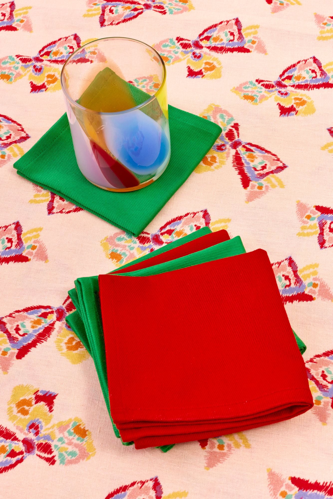 Red and green napkins on a colorful rain-bow patterned tablecloth with a glass.