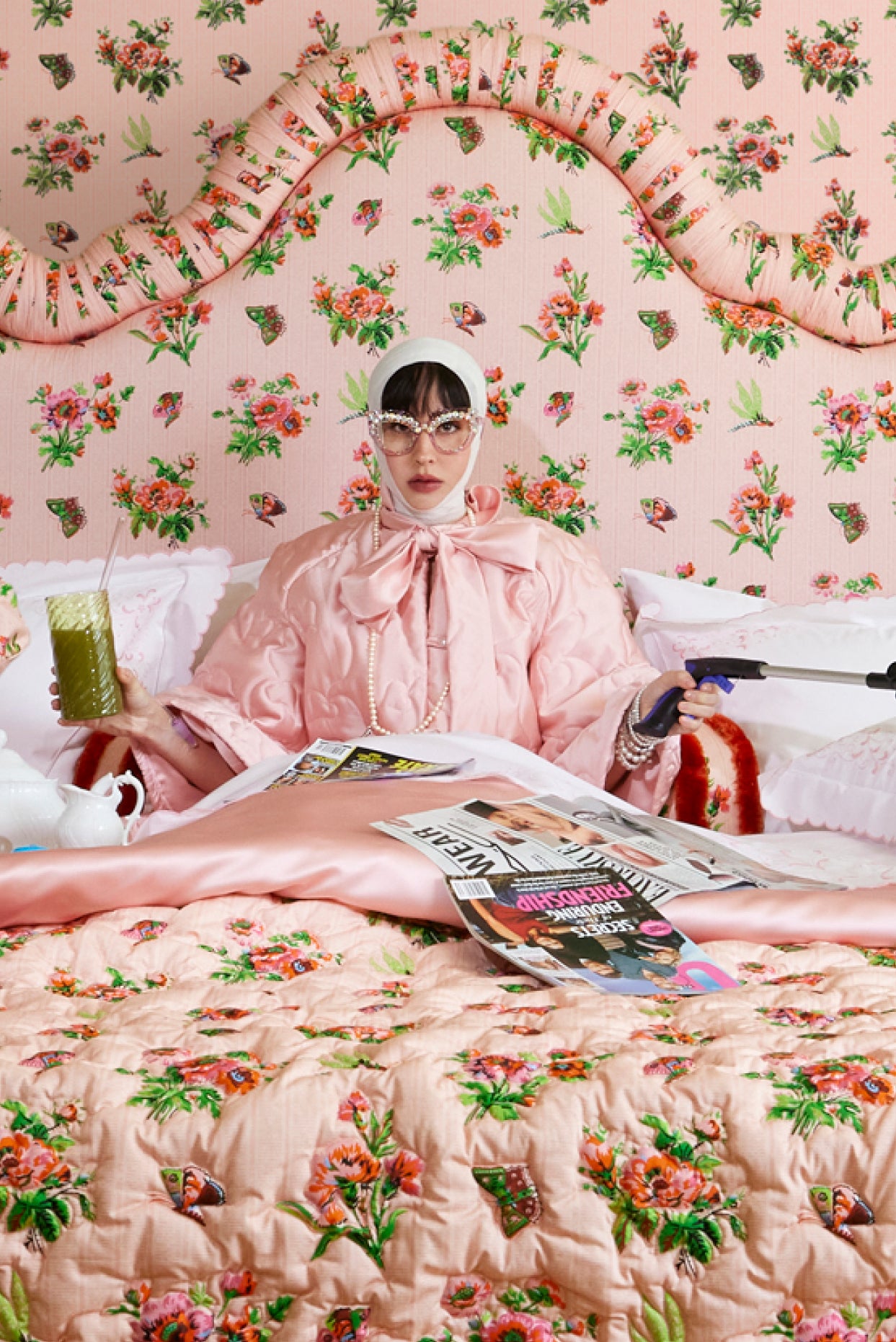 Person wearing a pink quilted house coat in a room with pink chintz wallpaper, quilt, and headboard.