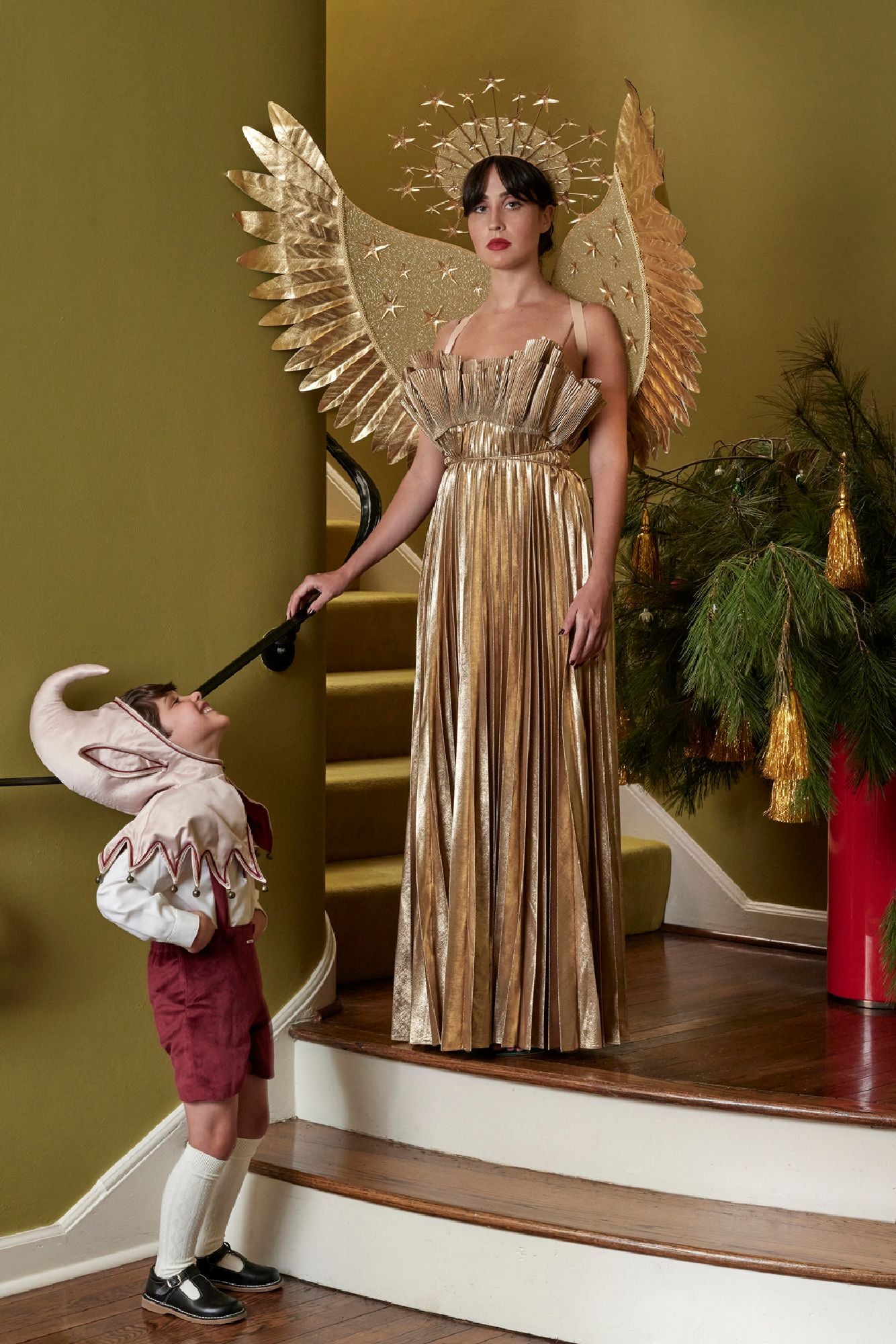 Woman in angel costume holding a child on a staircase with festive decorations.