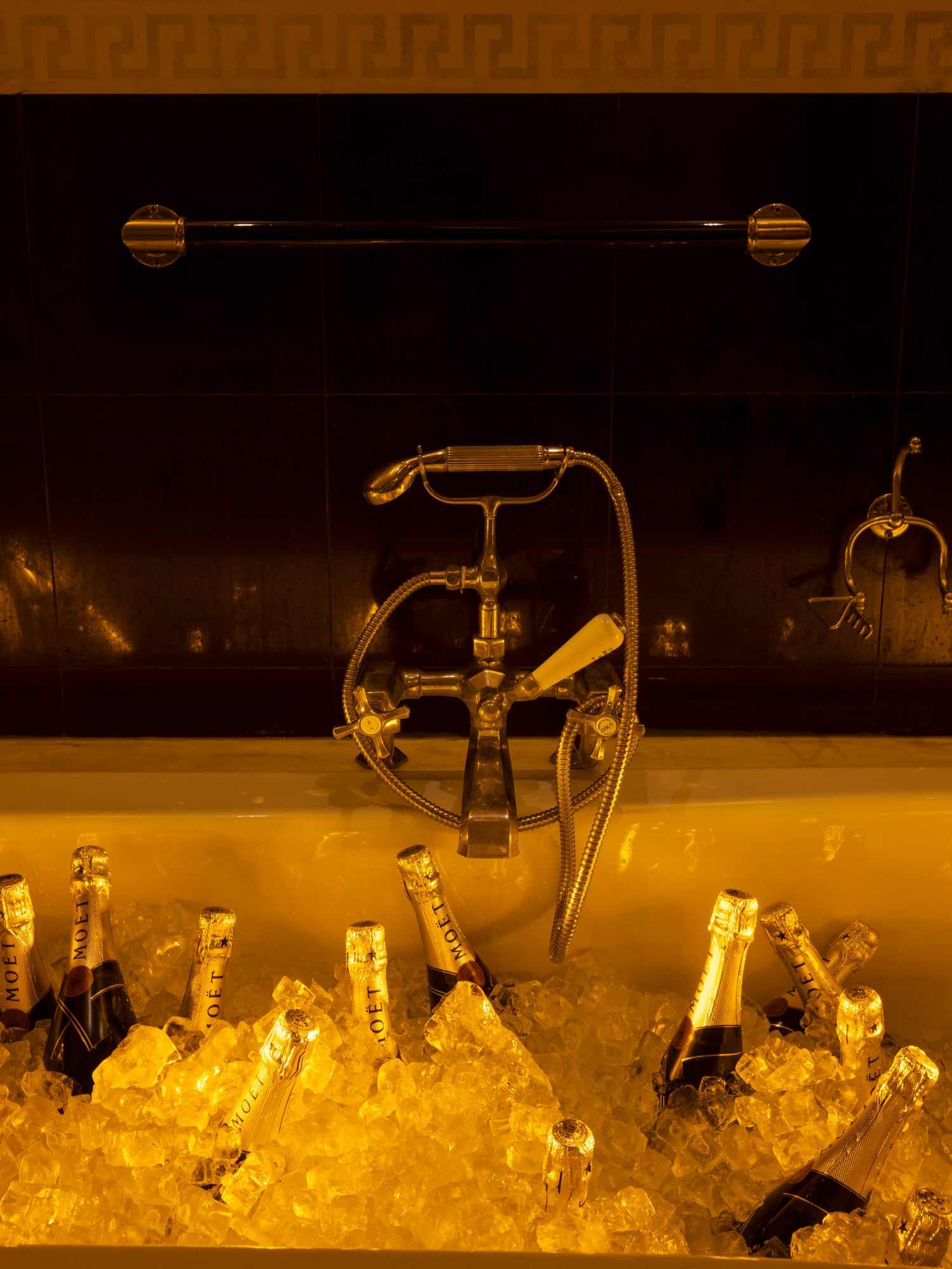Luxurious bathtub filled with ice and Moët champagne bottles, featuring elegant brass vintage-style fixtures against dramatic black tile – an indulgent champagne service setup for an extravagant celebration.