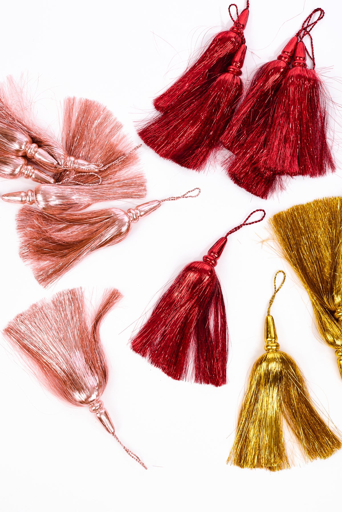 6 metallic tassel embellishments in rose gold, burgundy, and gold, arranged on a clean white background.