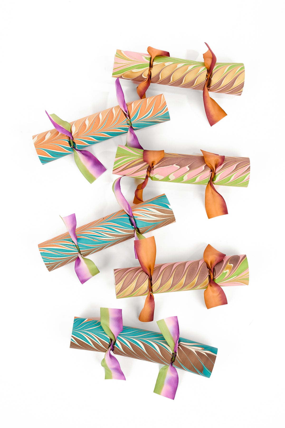 Six cylindrical party crackers with colorful abstract marbled patterns in fall colors, tied with matching ribbon bows, arranged vertically on a white background.