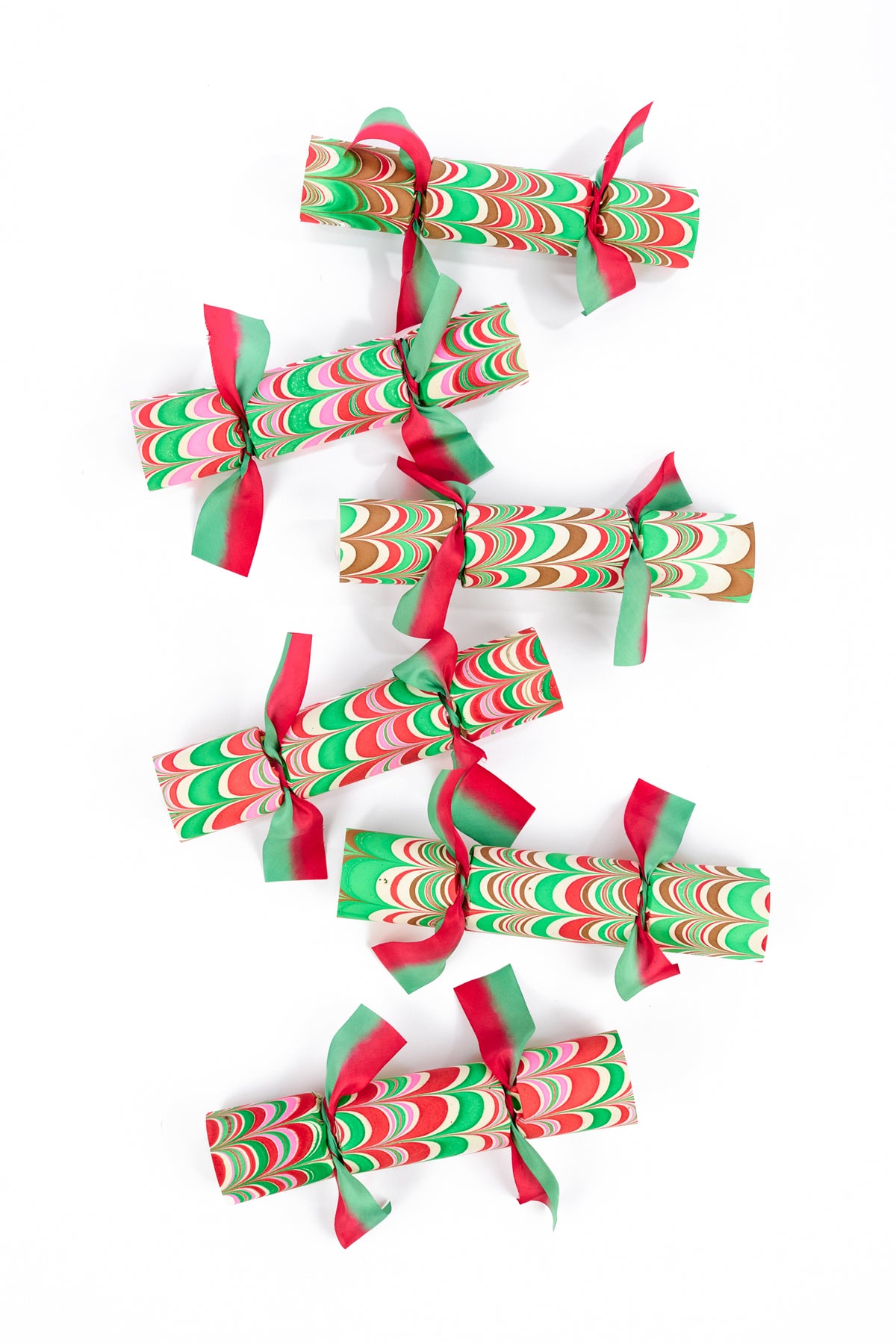 Six Christmas-themed paper cracker ornaments with red and green marbled patterns and ribbon ties, arranged vertically on a plain white background.