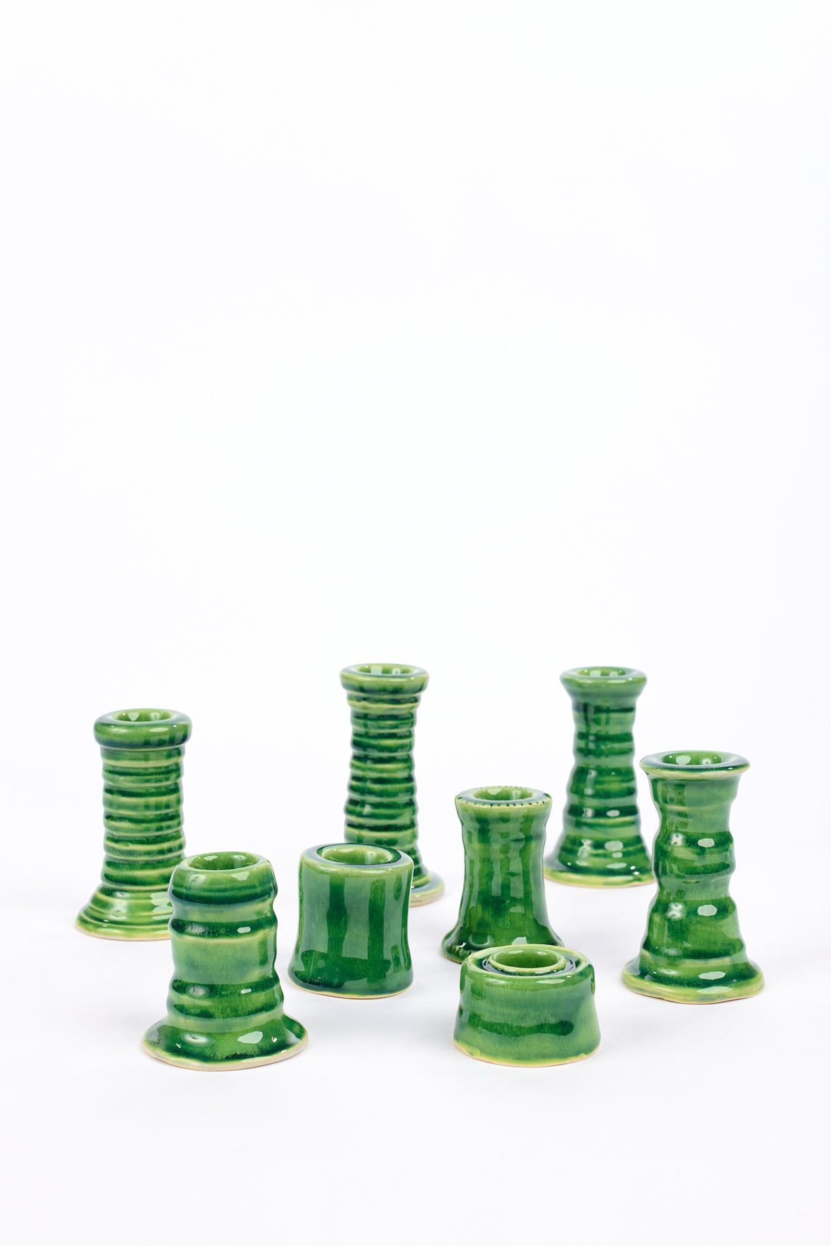 A set of eight small green ceramic candle holders with ribbed and tiered designs, arranged on a plain white background.