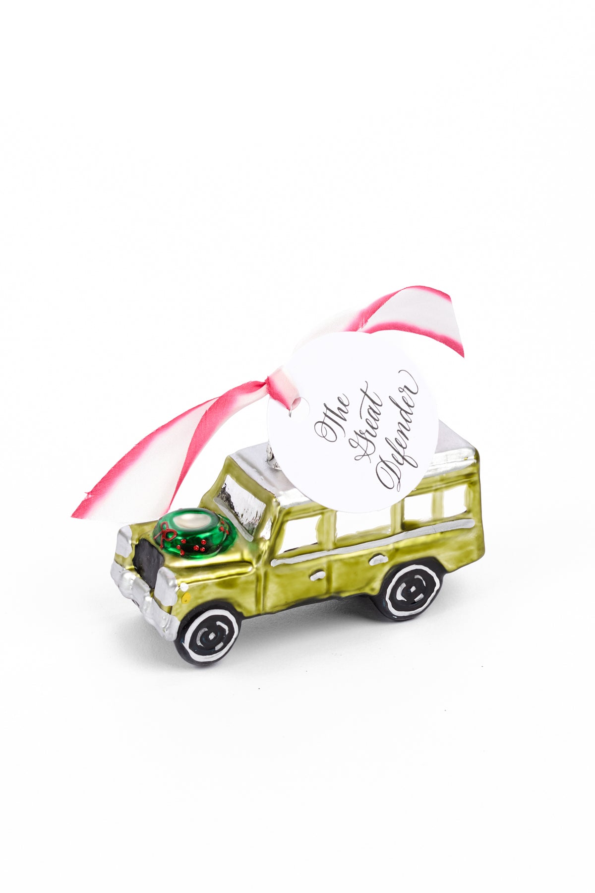 A small metallic green truck ornament with a pink ribbon and a white hanging tag that reads 'The Great Defender' on a plain white background.