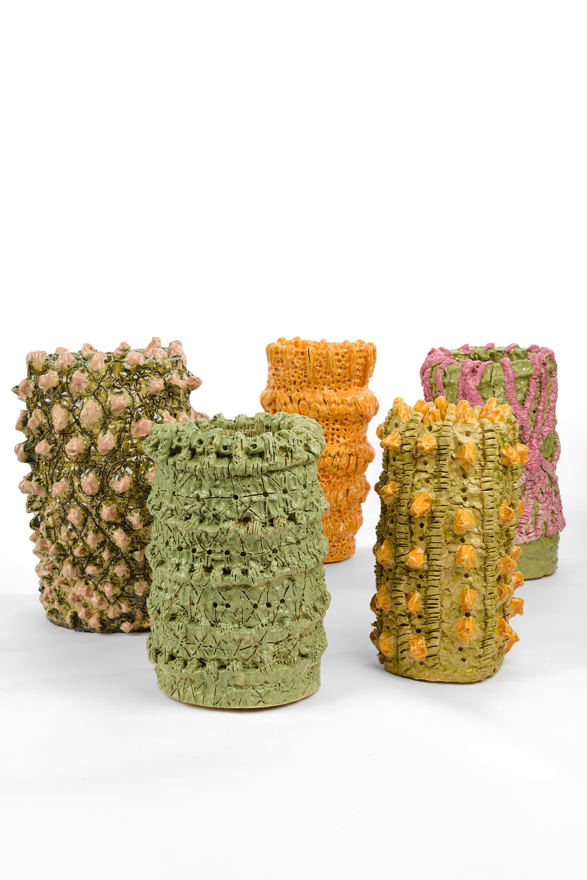 Group of five cylindrical ceramic vases with irregular hand-built surfaces and glossy glazes. The vases feature raised textures in combinations of pale green, olive, orange, pink, and dark green, including floral buds, looping bands, ridges, holes, and layered clay details.