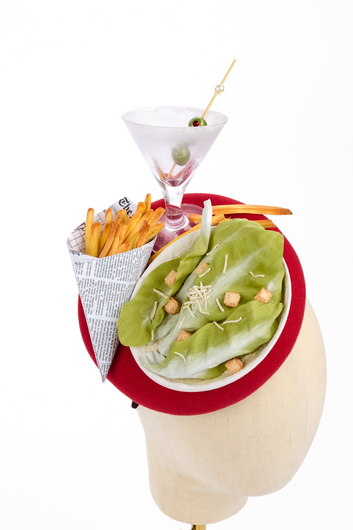A novelty hat shaped like a head, featuring a red brim , displayed on a mannequin head against a white background. The hat is decorated with a white plate of caesar salad, french fries, a martini glass with an olive.
