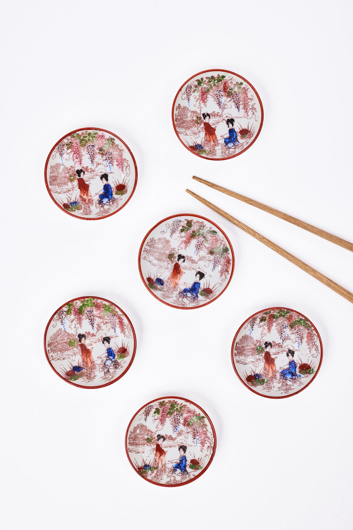Five round dishes with traditional Chinese-style illustrations of figures in red and blue robes under pink blossoms, arranged on a white background alongside a pair of wooden chopsticks.