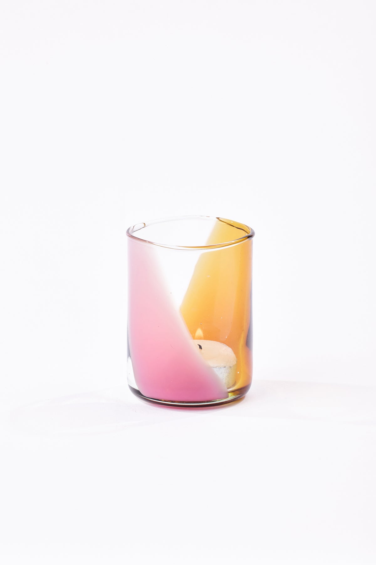 A clear glass candle holder with a pink and orange gradient design, containing a small white tea light candle, set against a plain white background.