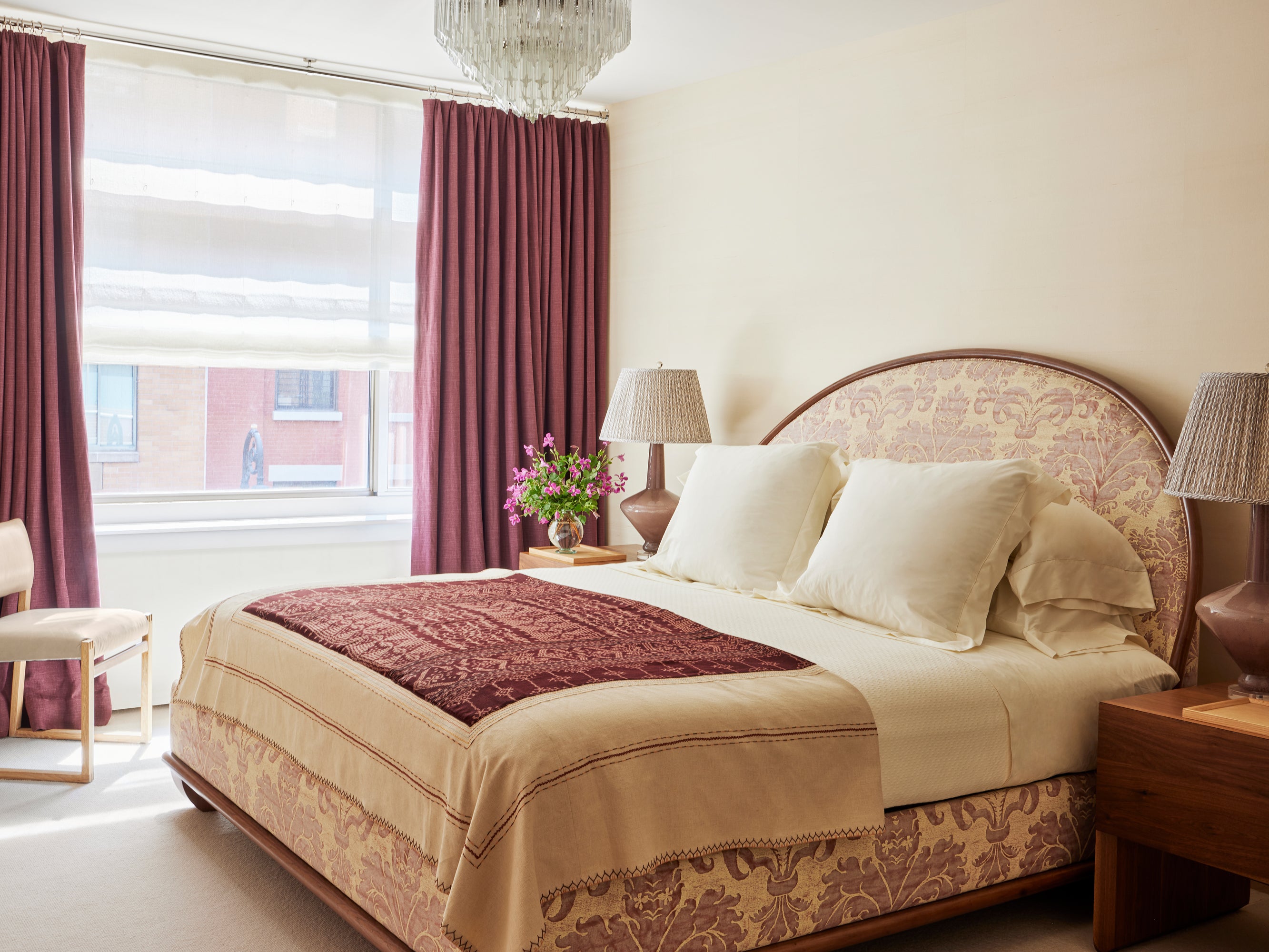 "Elegant master bedroom featuring a harmonious palette of mulberry and cream with a damask-upholstered bed frame, coordinating drapery, and crystal chandelier – demonstrating Houses & Parties' sophisticated approach to creating restful yet refined spaces through consistent color story, luxurious textiles, and carefully considered proportions.