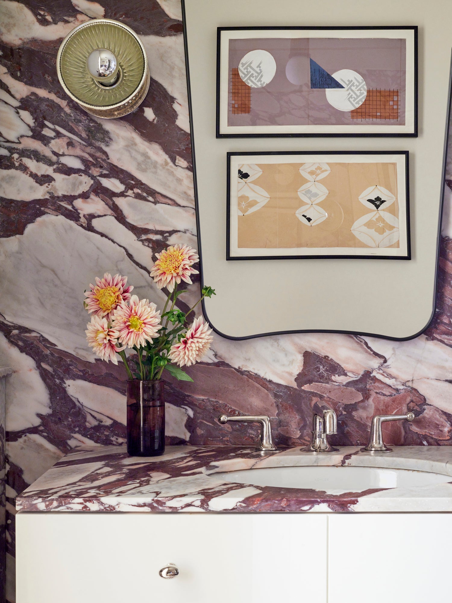 Sophisticated powder room design showcasing dramatic burgundy-veined marble dramatically matched to create a continuous pattern, complemented by modernist geometric artwork, polished nickel fixtures, and a simple arrangement of fresh dahlias – exemplifying Houses & Parties' expertise in elevating small spaces through bold natural materials and refined artistic elements.