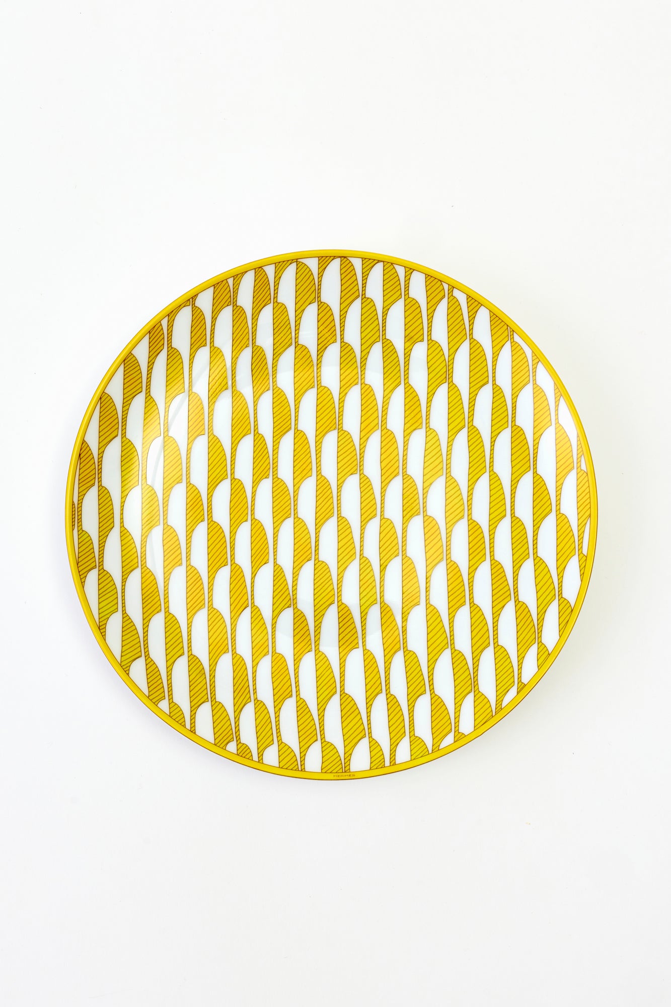 This architectural design by Arielle de Brichambaut for Hermès is intensely ablaze, its graphic forms radiating with warmth. The subtle variation in shades of yellow and the cross-hatched contours give depth to this ode to summer. Convivial, carefree, and even more beautiful in person - just like you. Fine porcelain. Made in France.