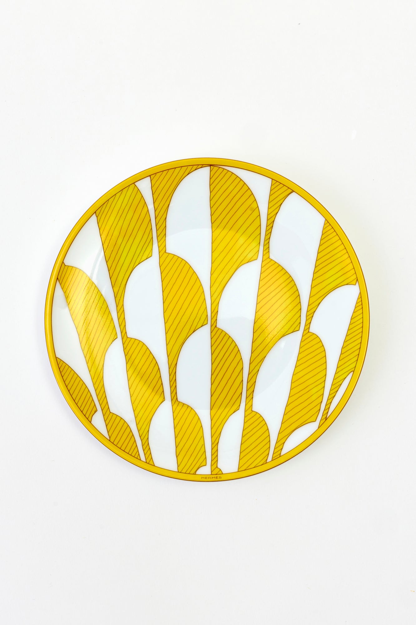 This architectural design by Arielle de Brichambaut for Hermès is intensely ablaze, its graphic forms radiating with warmth. The subtle variation in shades of yellow and the cross-hatched contours give depth to this ode to summer. Convivial, carefree, and even more beautiful in person - just like you. Fine porcelain. Made in France.