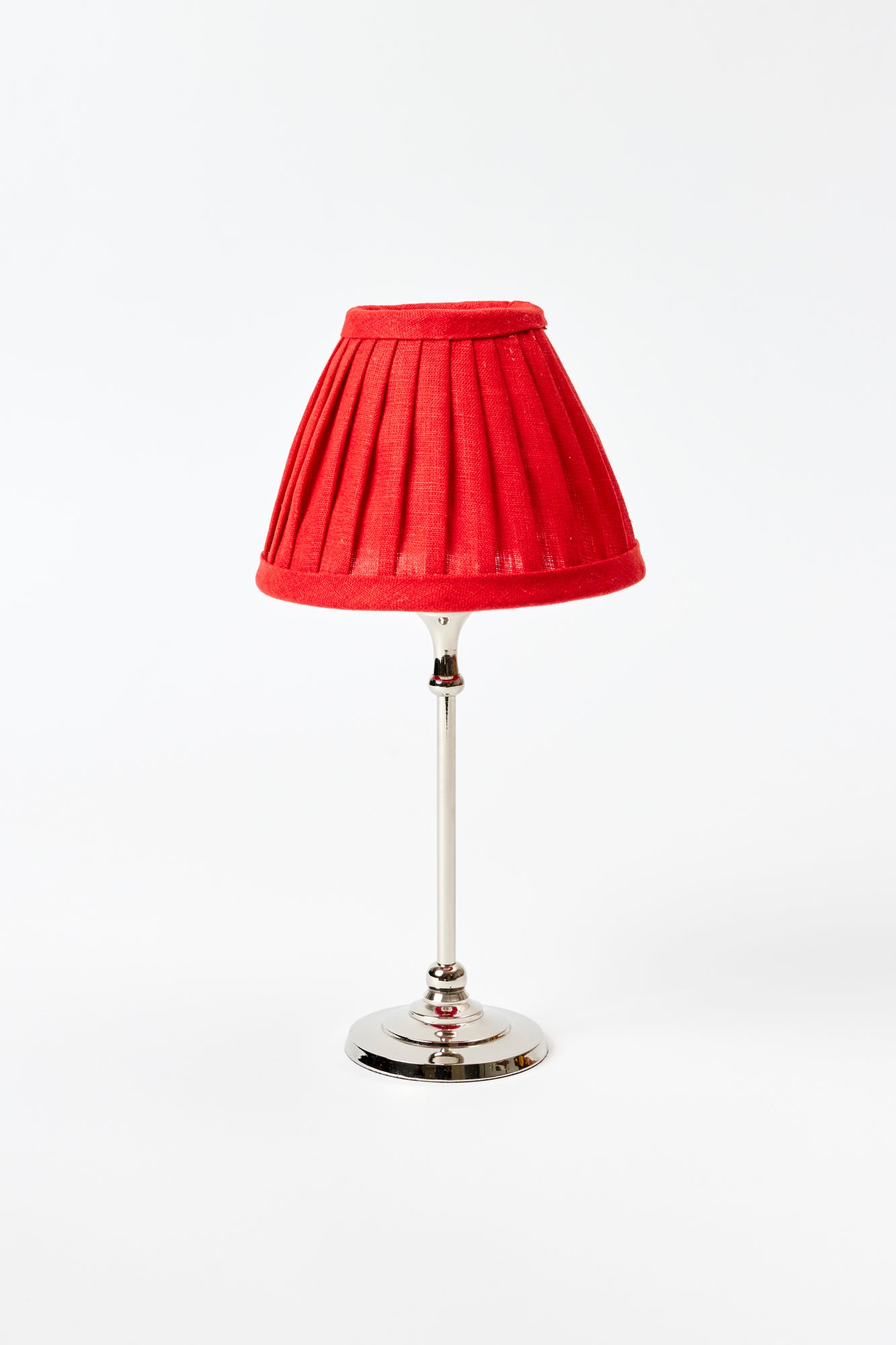 Small table lamp against a white background. Chrome colored lamp base with a bright red pleated silk lamp shade.