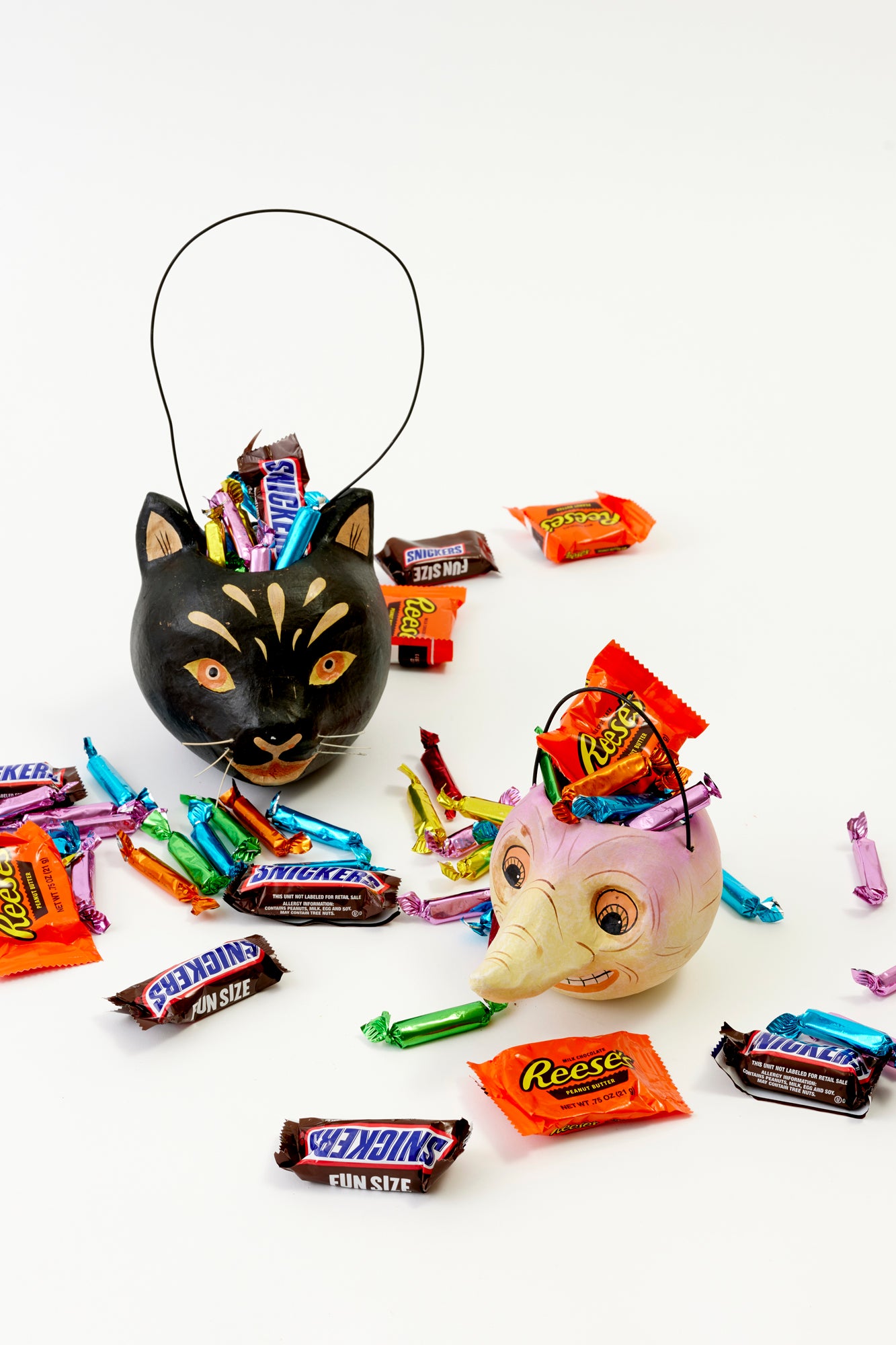 A small, black candy bucket shaped like a cat with various colorful candies spilling out of it, placed on a white background.