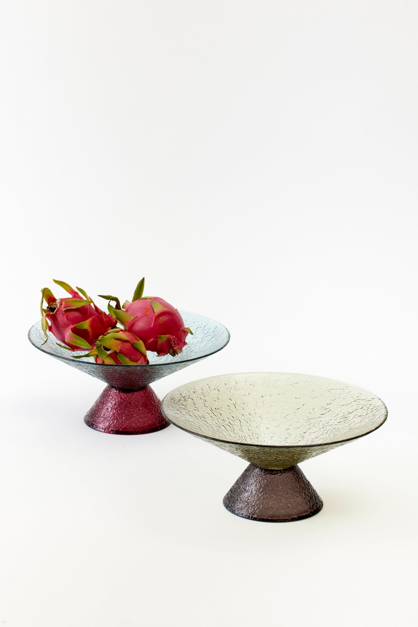 Contemporary glass pedestal dishes with a textured surface, in soft pastel shades of teal and rose, elegantly displaying vibrant dragon fruit. A blend of luxury and minimalism for stylish entertaining.