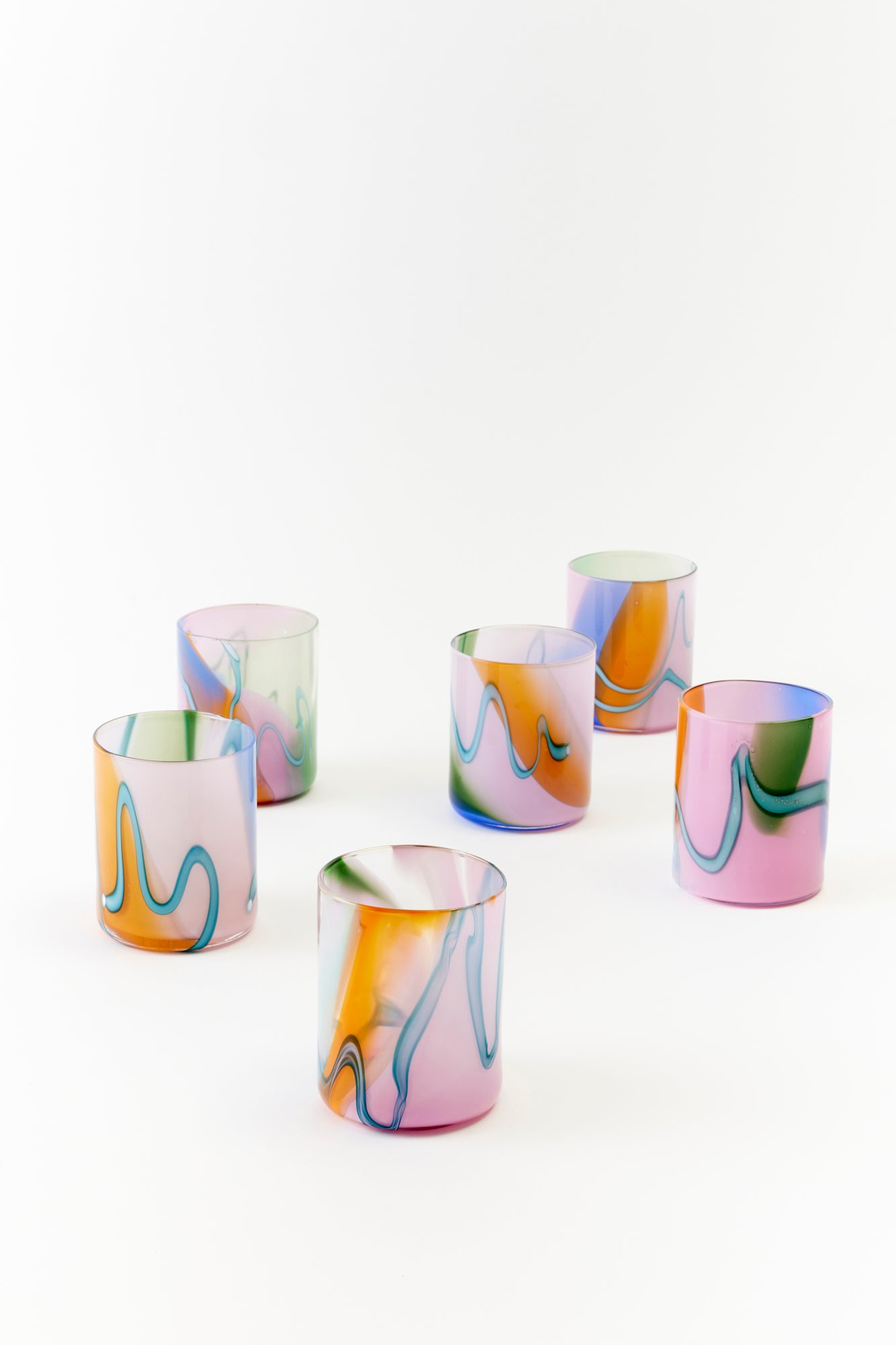 Set of six artfully designed tumbler glasses featuring a pastel color palette with wavy, marbled swirls of blue, pink, green, and amber. These unique hand-blown glasses bring a modern, artistic touch to any table setting, perfect for adding a pop of color and elegance to everyday dining or special occasions.
