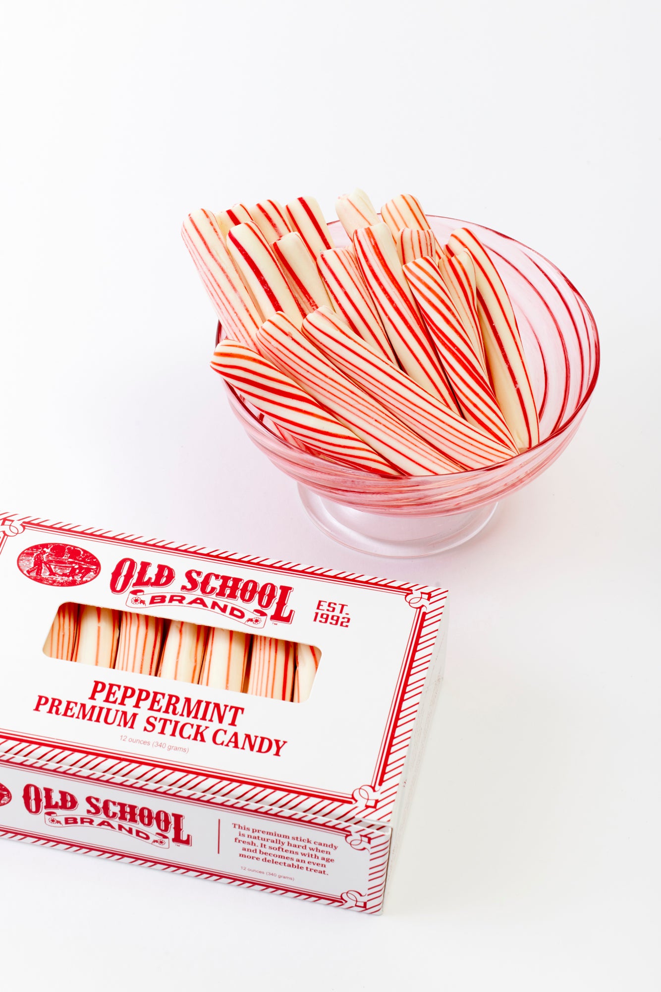 A clear bowl filled with striped peppermint sticks, accompanied by a classic white and red "Old School Brand" box of peppermint premium stick candy. The candy’s red stripes and nostalgic packaging evoke a festive and traditional holiday feel.