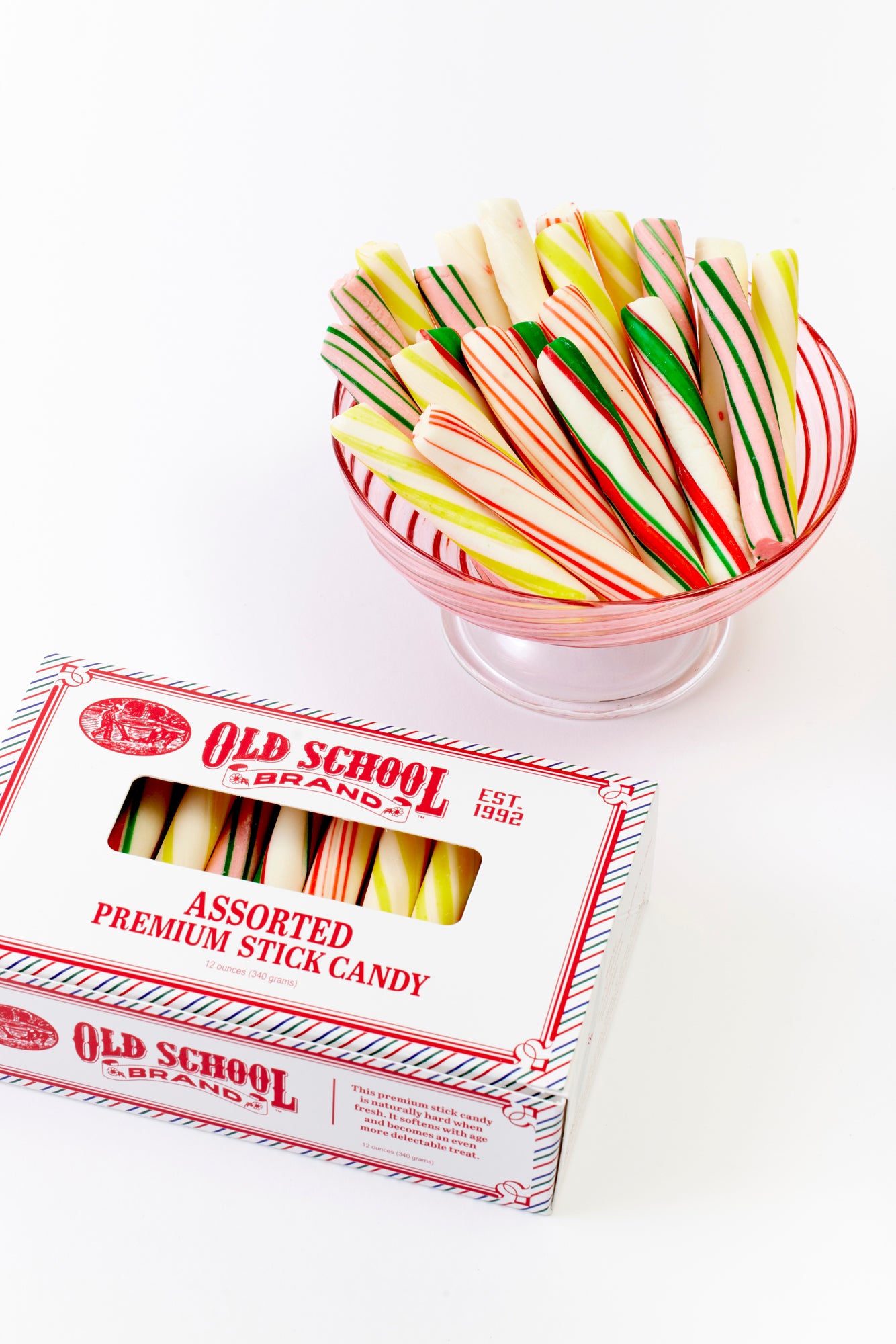 A clear bowl filled with colorful assorted premium stick candy featuring stripes in shades of red, green, yellow, and white. Next to the bowl is a matching "Old School Brand" box, emphasizing the fun variety and vintage charm of the sweet treat.