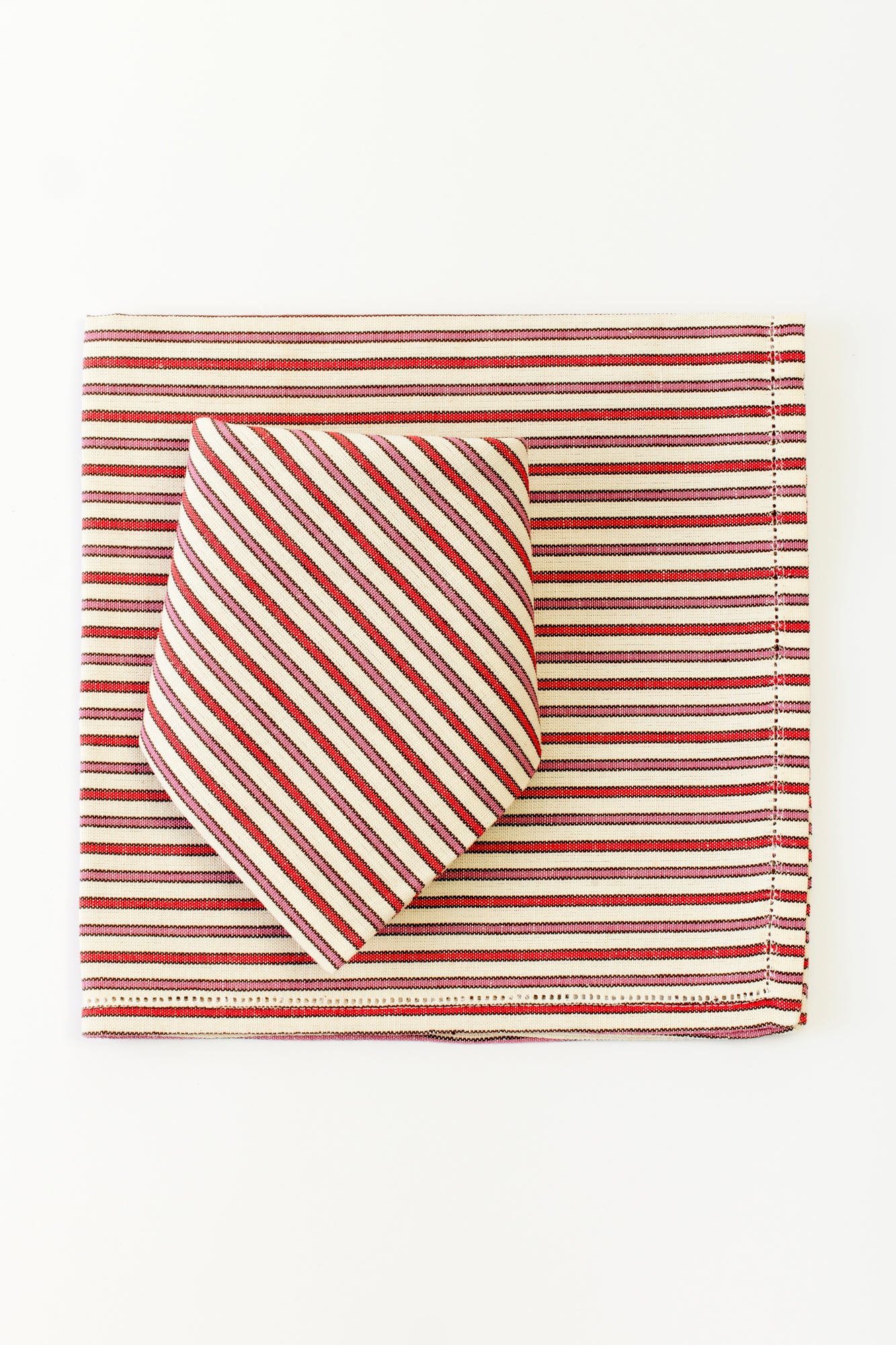 A striped fabric set, including a rectangular placemat and a folded napkin on top. Both the napkin and placemat feature a pattern of alternating red, black, and white horizontal stripes, with the napkin arranged in a diagonal fold that contrasts the direction of the stripes on the placemat. The simple and neat arrangement emphasizes a coordinated, elegant table setting.