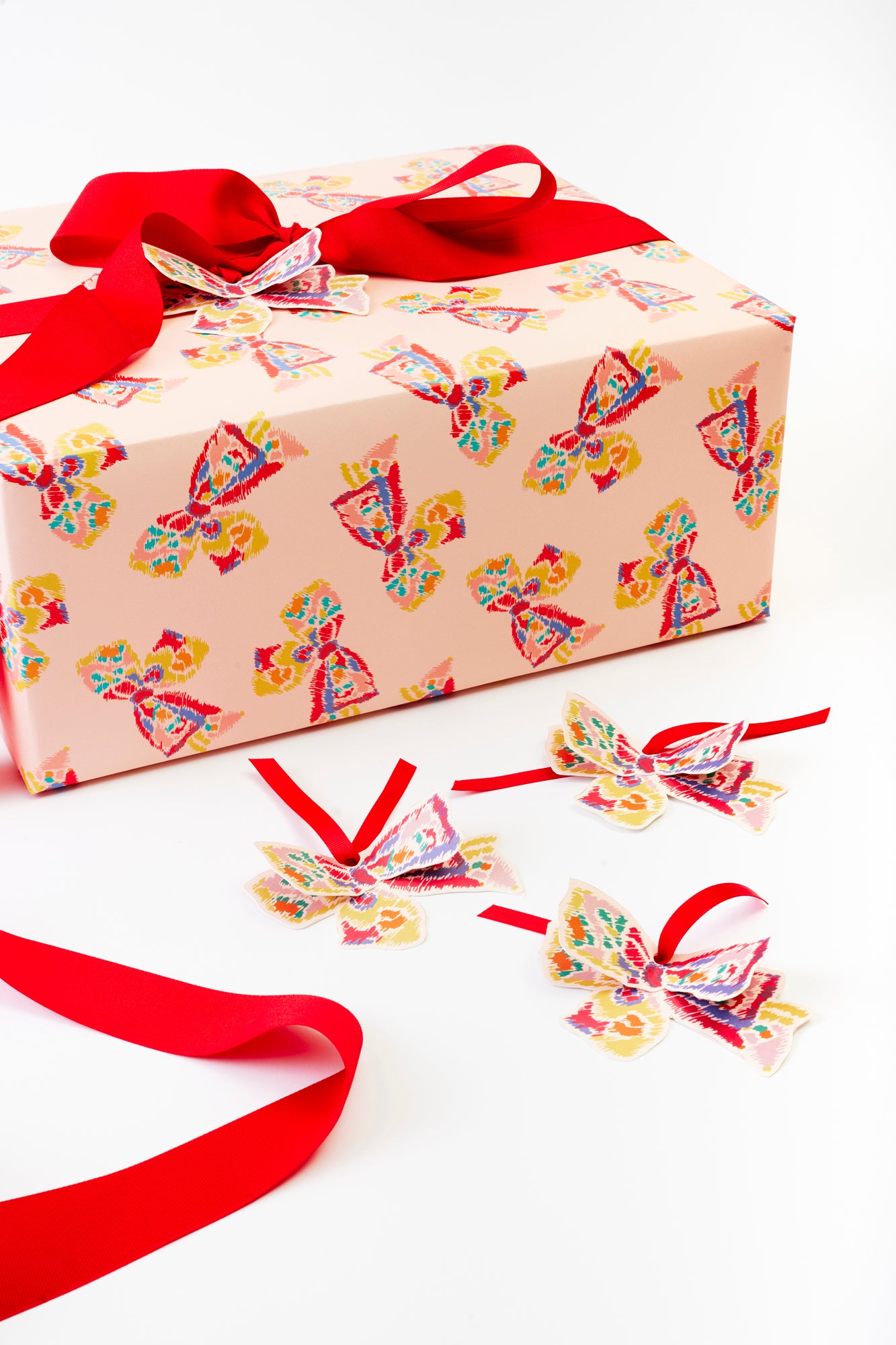 Colorful butterfly-patterned bows with red ribbons placed next to matching gift wrap.