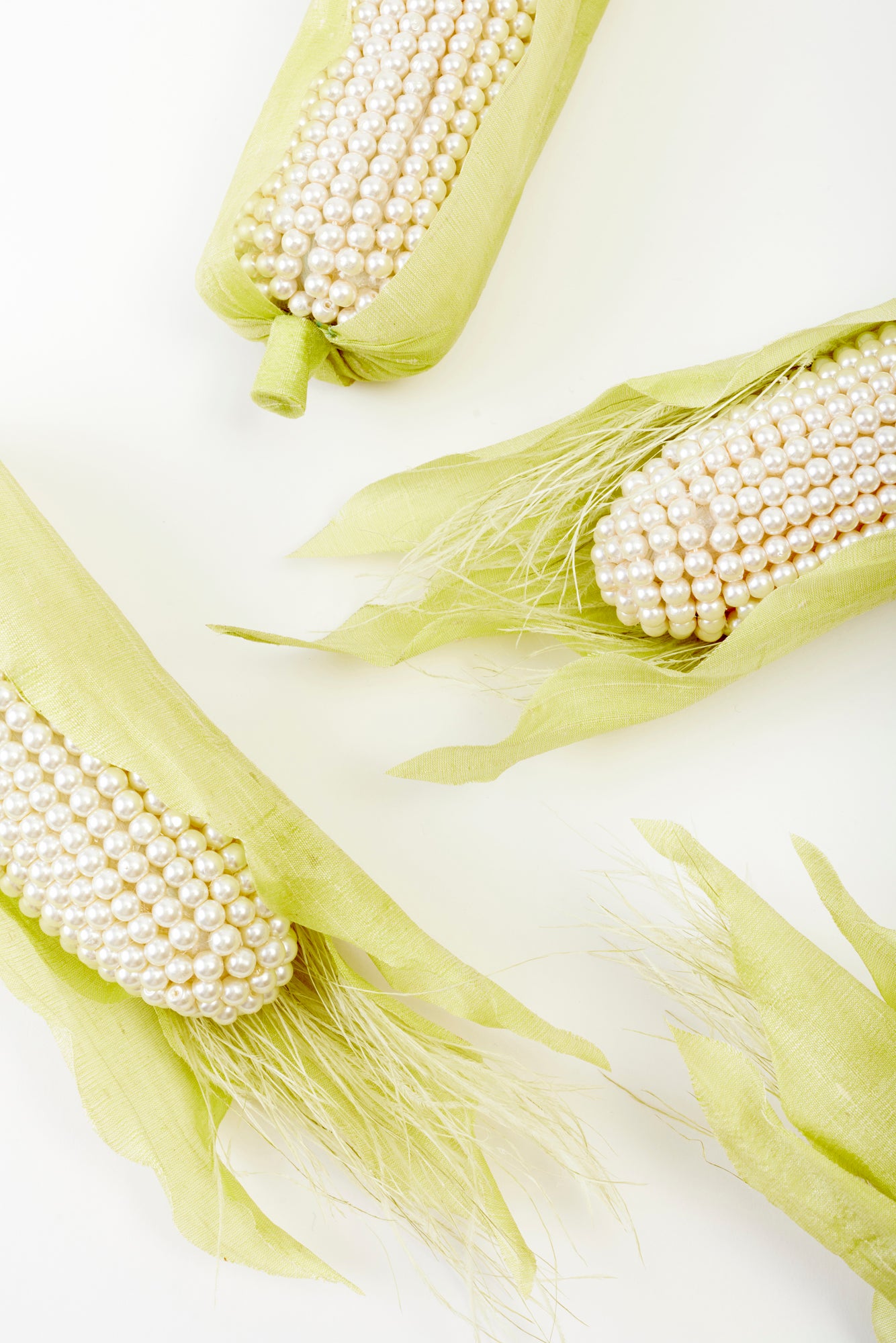 Pearl-adorned ears of corn nestled in vibrant green husks, a striking fusion of high fashion and natural beauty. These playful yet sophisticated decor pieces add a couture touch to any room.