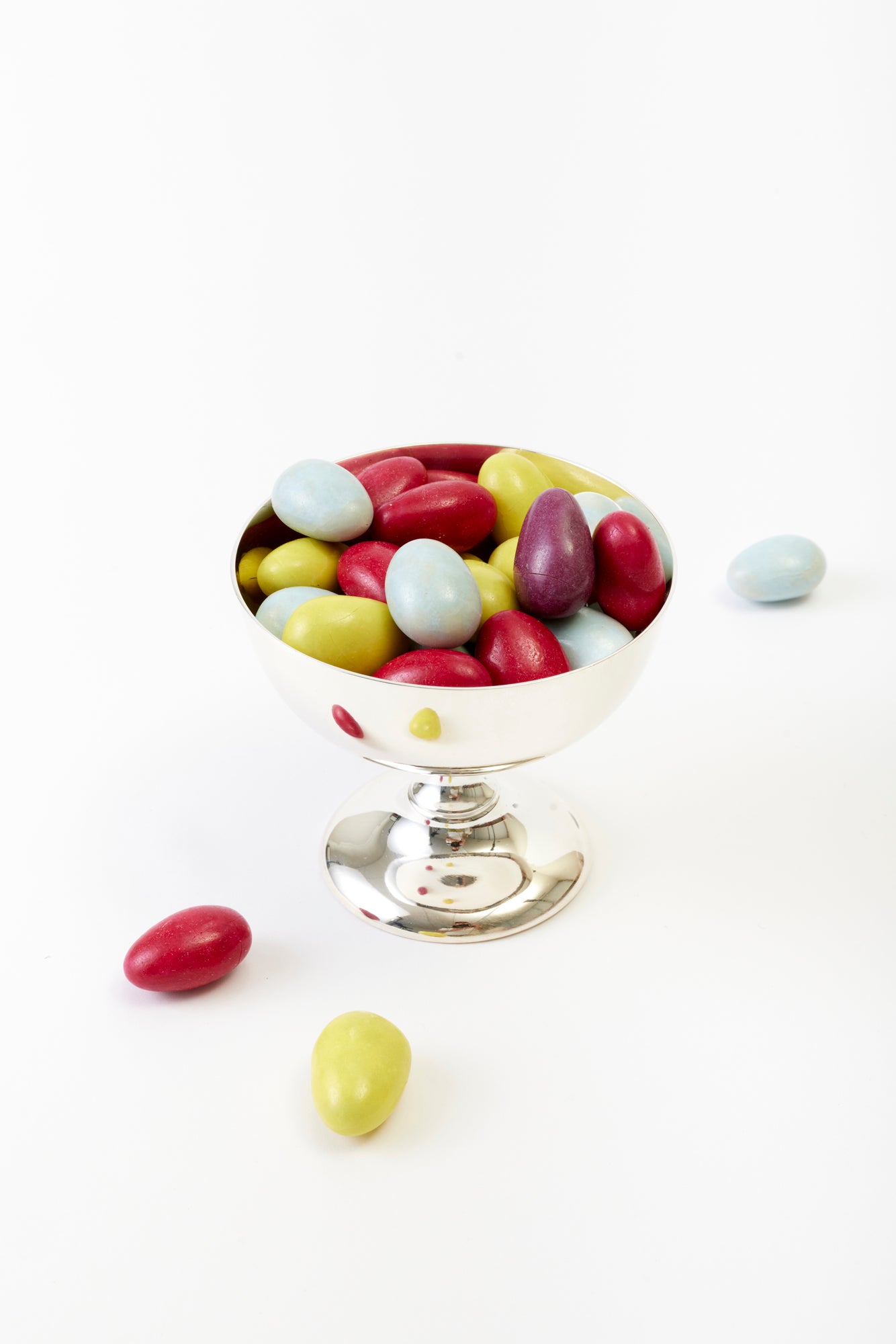 A refined silver bowl brimming with colorful coated almonds in hues of red, lime, and pale blue.