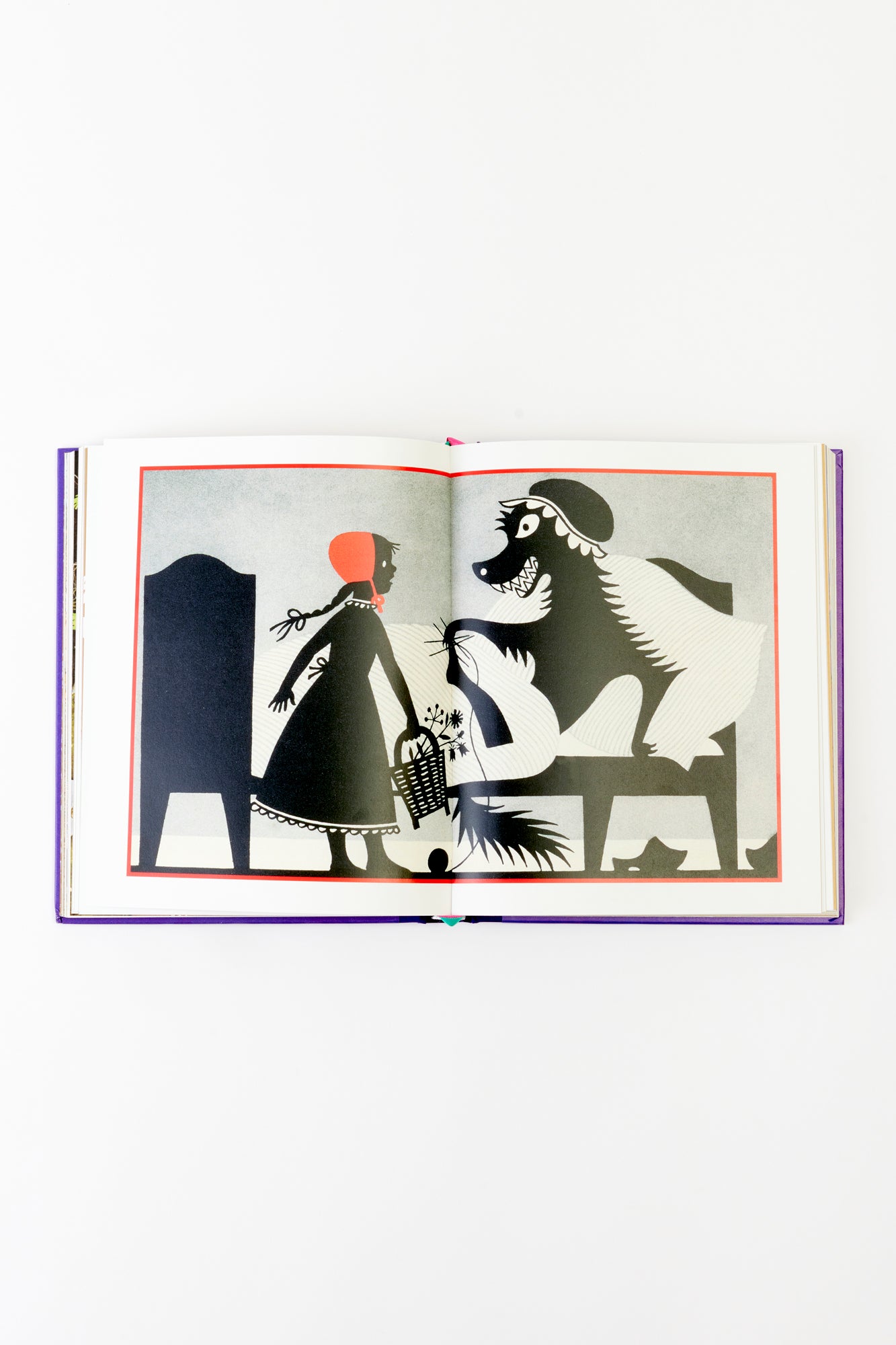 An open spread from The Fairy Tales of the Brothers Grimm showcasing a striking black-and-white illustration of Little Red Riding Hood facing the Big Bad Wolf. The sharp, minimalistic art brings an iconic fairy tale moment to life.