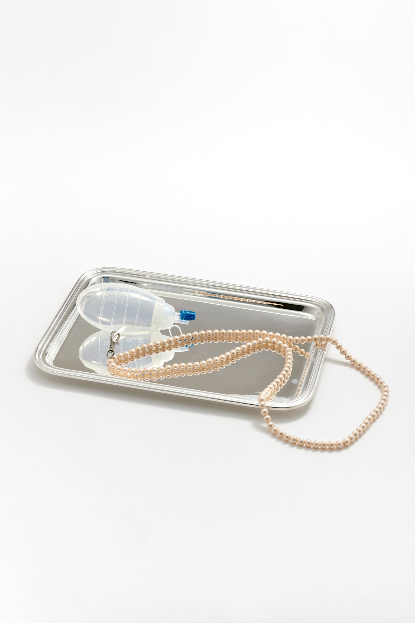 Pearl lanyard attached to surgical drain on a silver tray with a white background.