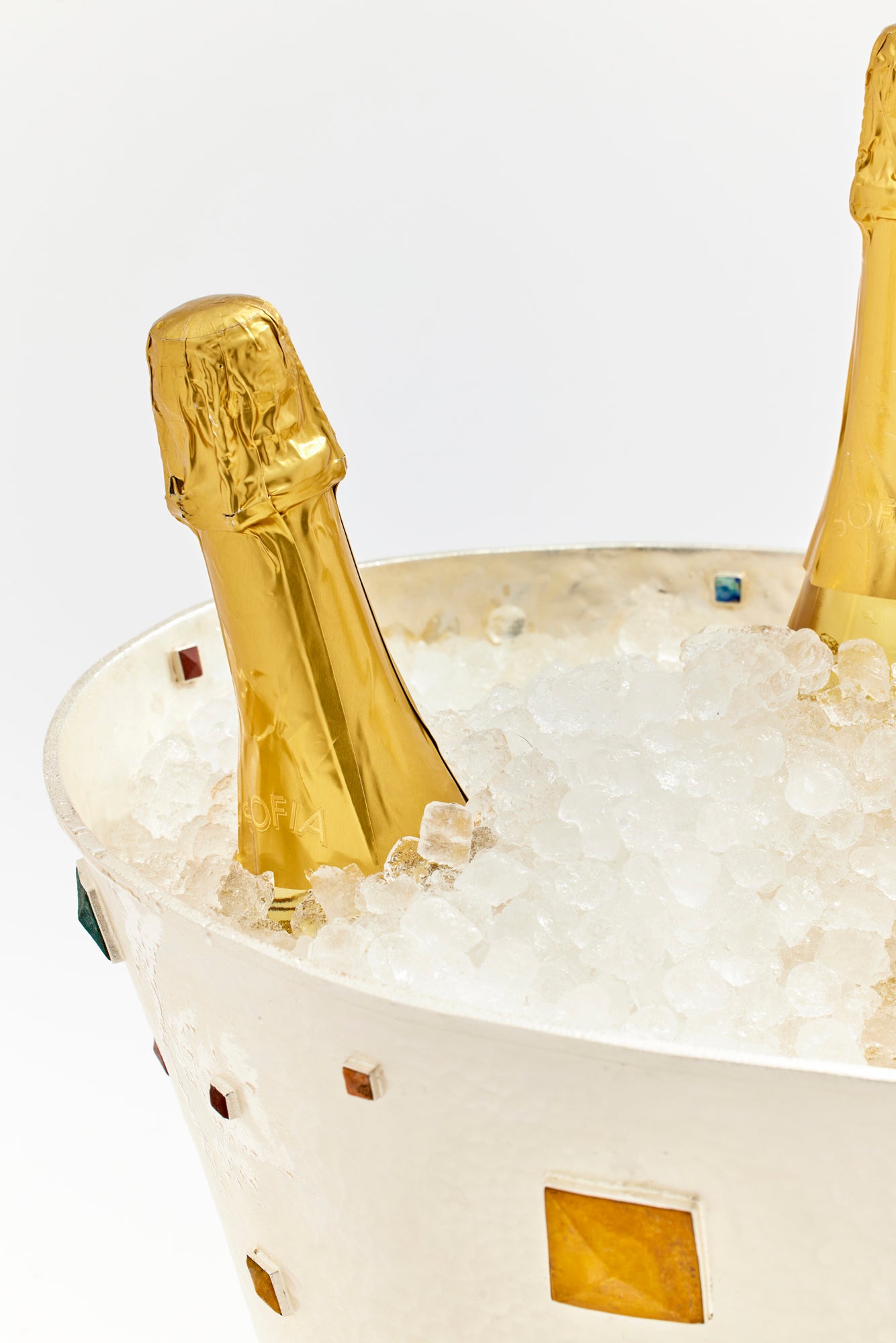 Close-up of a hammered silver ice bucket adorned with semi-precious stone inlays, filled with ice and showcasing a bottle of champagne wrapped in golden foil. The luxurious design and intricate gemstone details elevate the presentation, making it ideal for a sophisticated celebration or elegant entertaining.