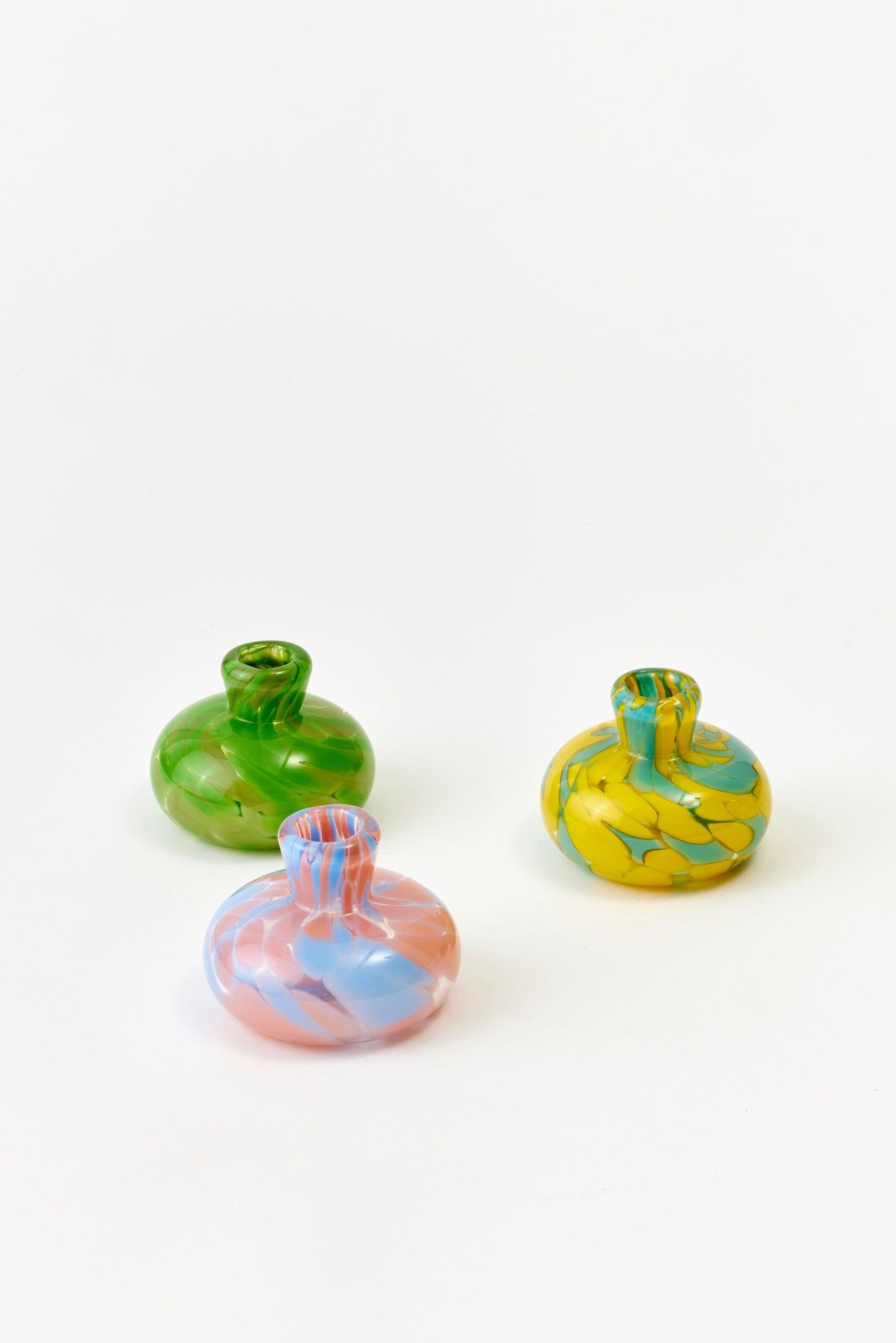 Three small glass candle taper holder vases with with colorful patterns on a white background