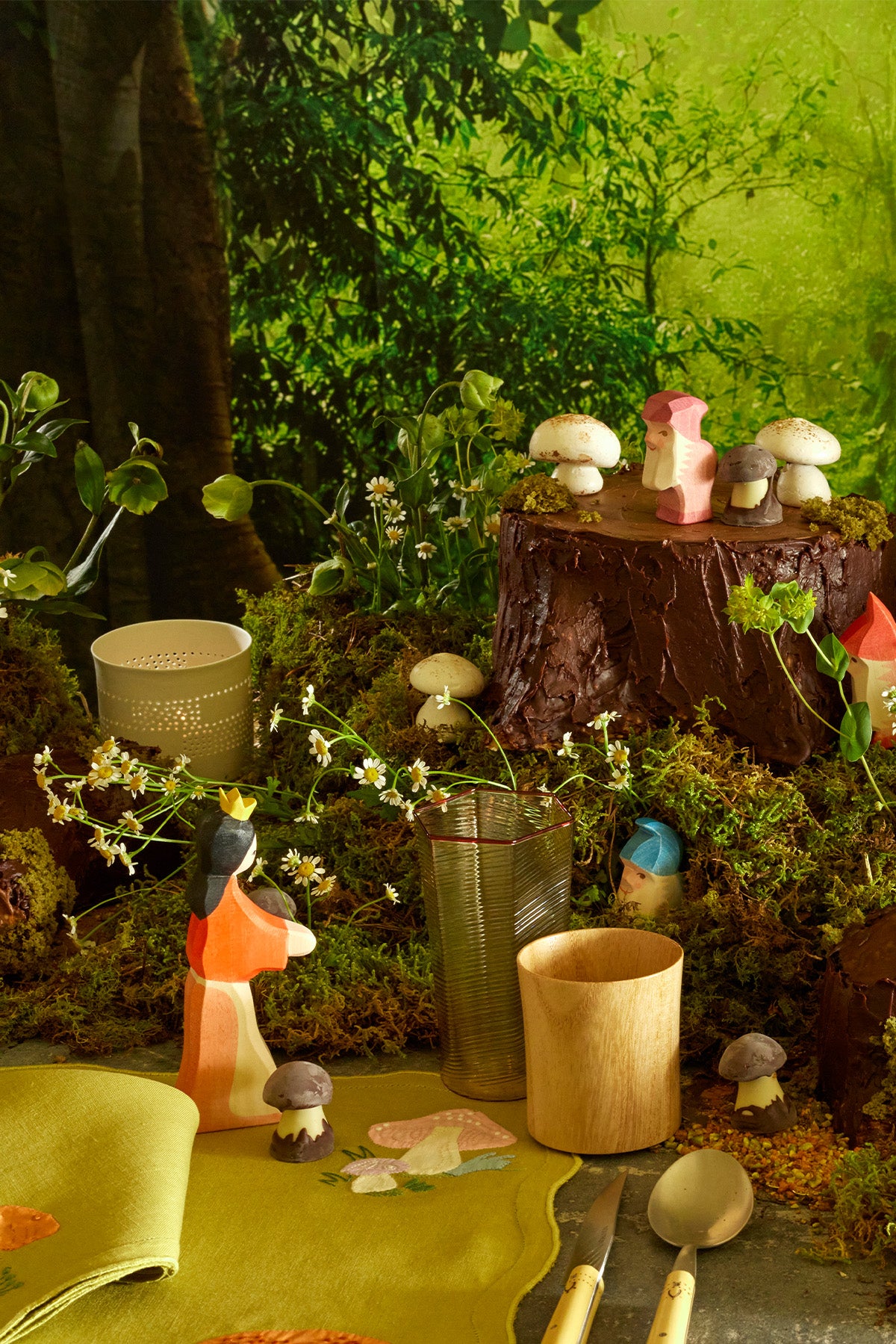 Whimsical fairy themed table setting featuring wooden tumblers made from Paulownia wood, wooden Snow White and the seven dwarves figurines, chocolate and caramel mushrooms, boxwood silverware, and linen placemats and napkins with French embroidered appliqué.