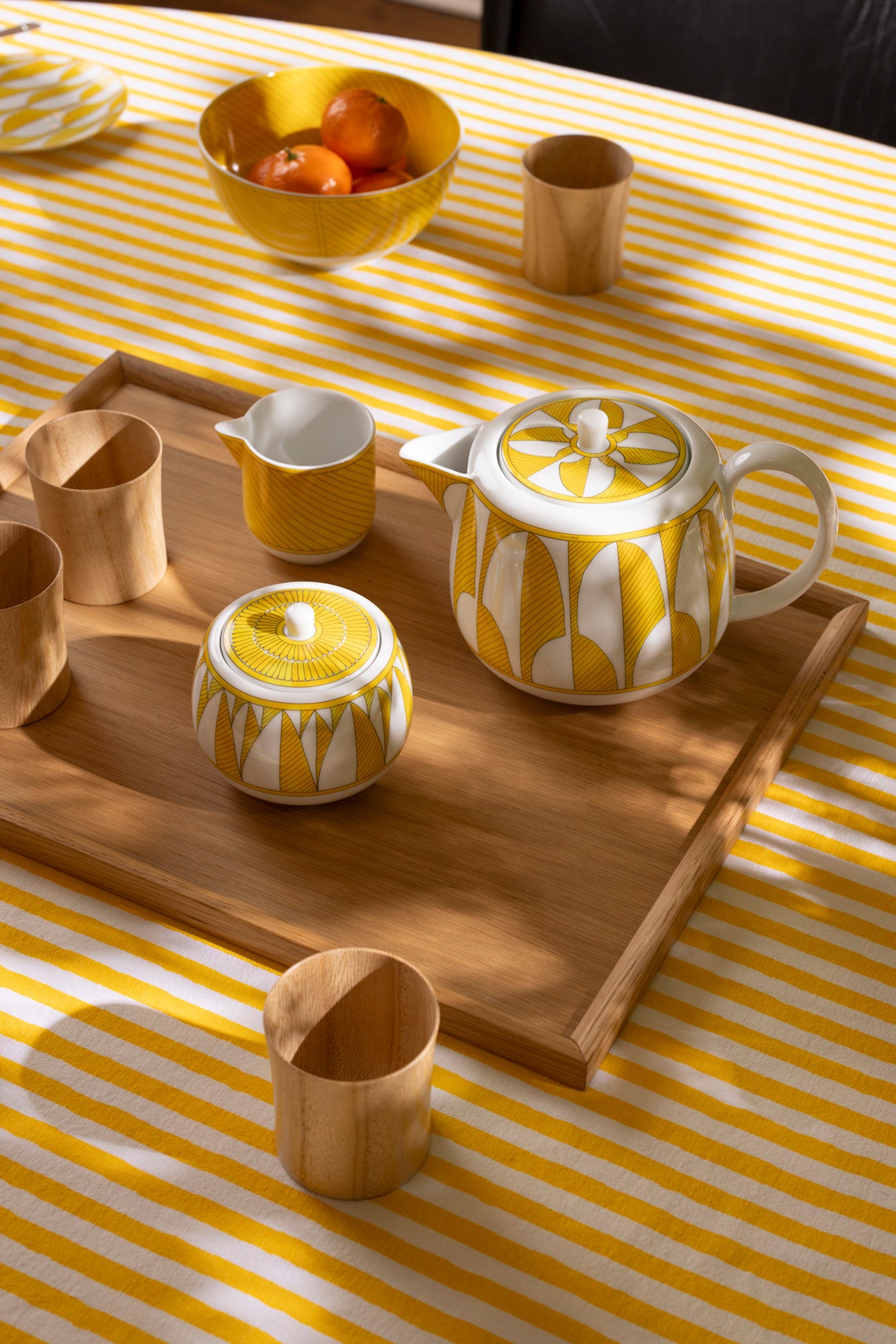 Photograph of a table setting featuring an oak wooden passing tray, yellow Hermes tea set, and wooden tumblers made from Paulownia wood.