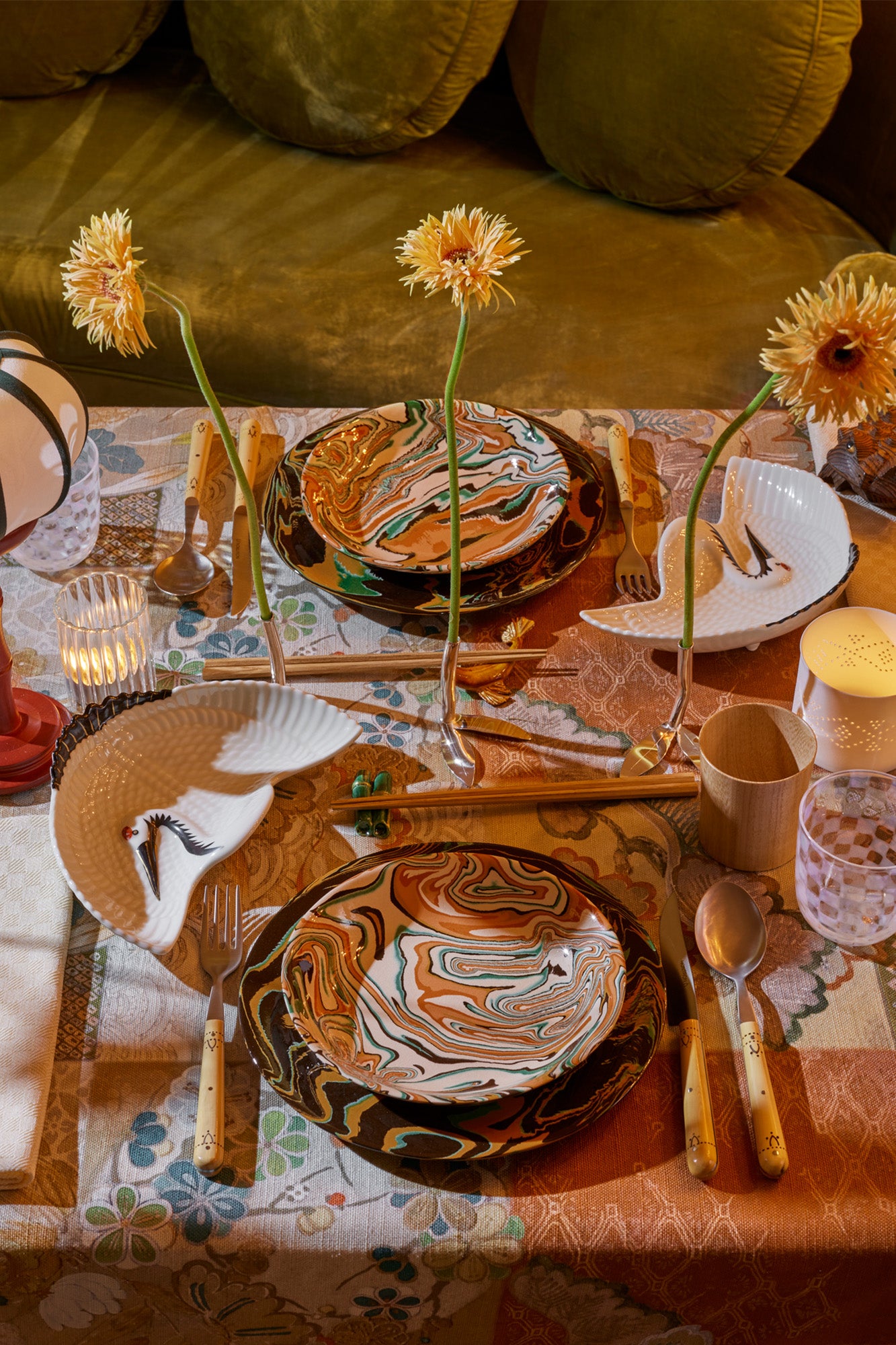 Marbled ceramic dishes and wooden tumblers set formally on a table with flowers and candles surrounding the tableware.