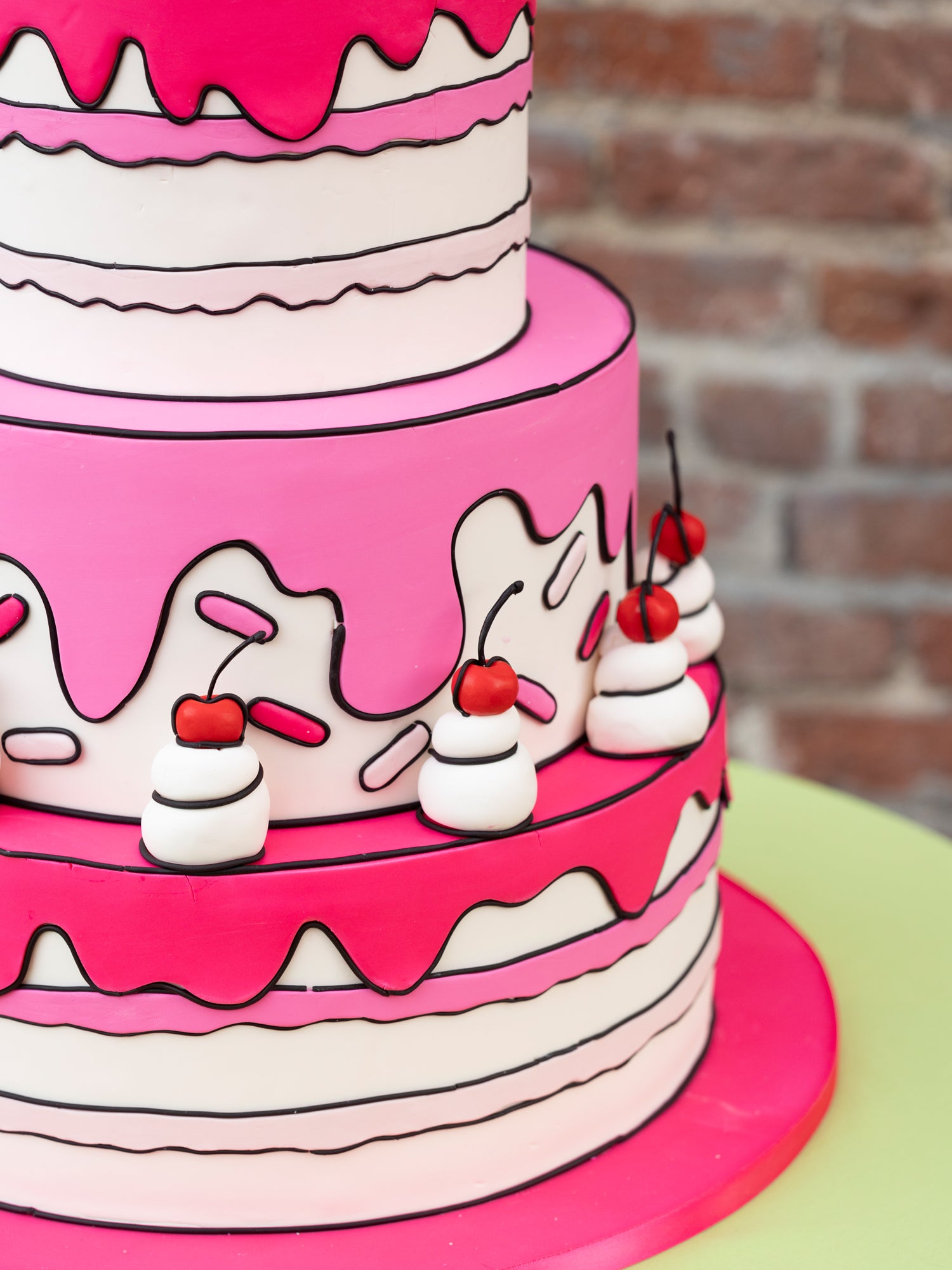Closeup of a pink and white cake with cherries and dark icing.