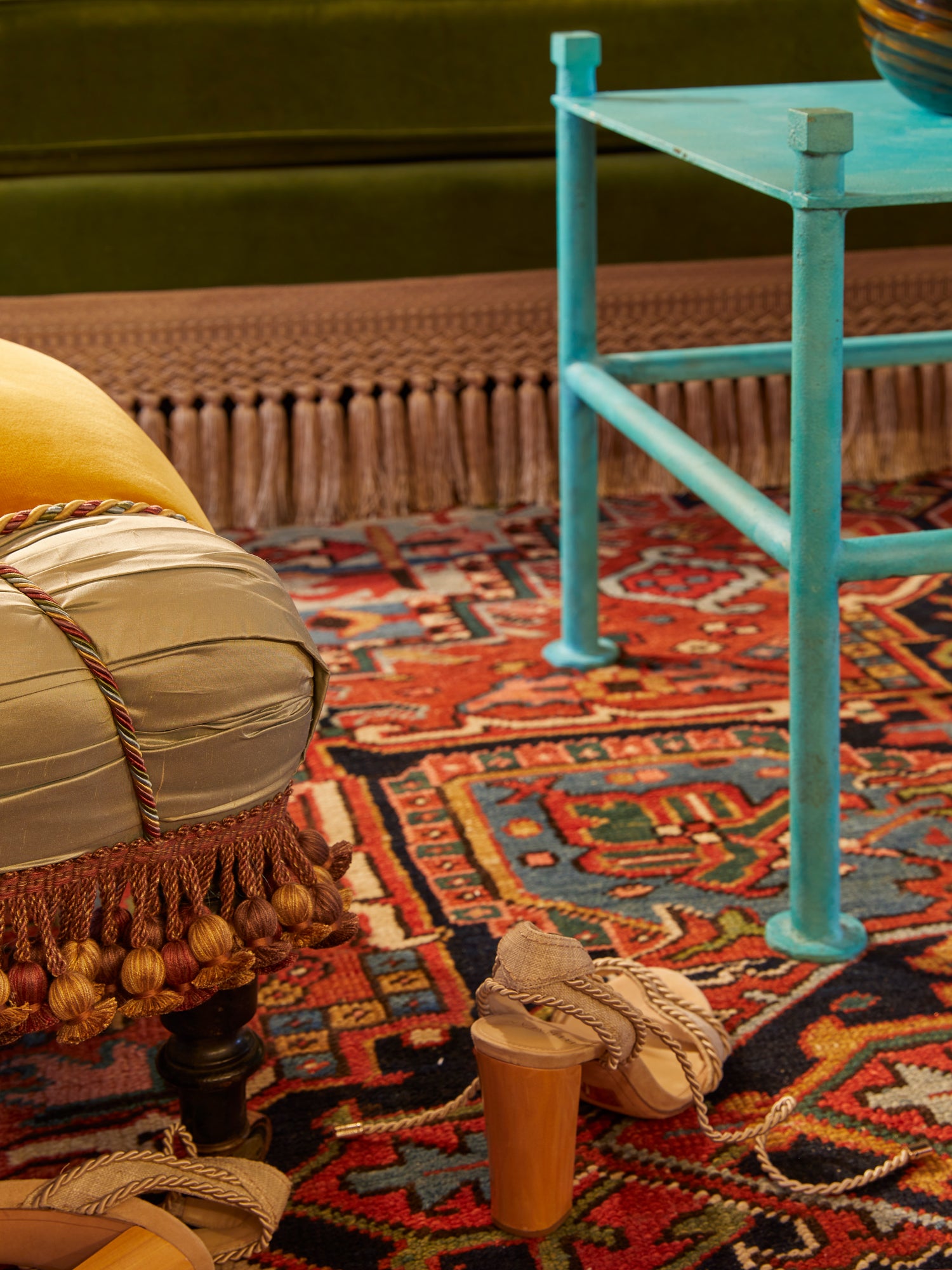 Artful interior detail showcasing exquisite craftsmanship through contrasting textures and finishes: a traditional Ottoman with tassel trim against a vibrant antique carpet, paired with a contemporary turquoise metal side table – illustrating Houses & Parties' signature approach of blending periods and styles for interiors with both historical richness and modern sensibility.