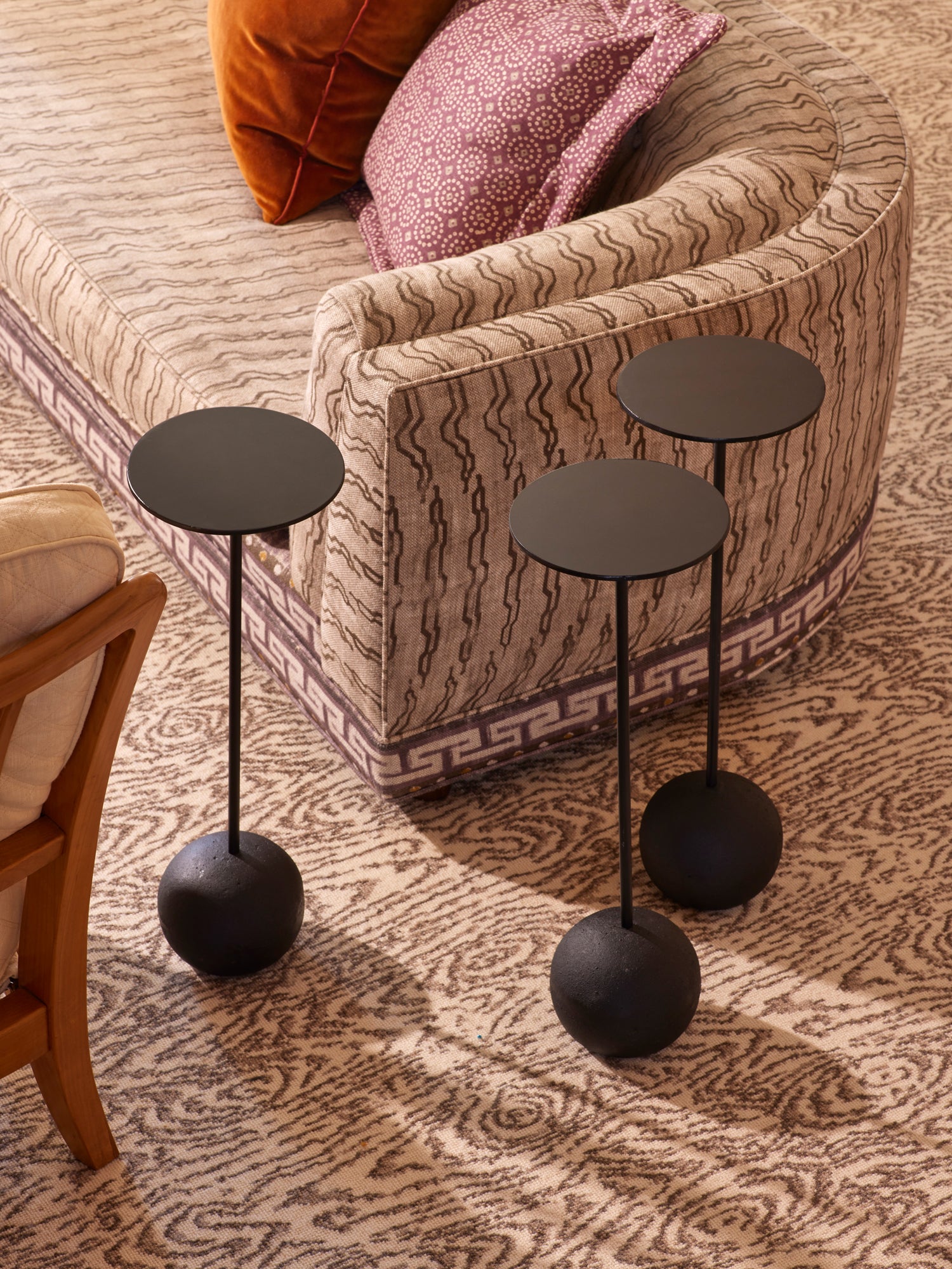 Elegant living room detail featuring a curved sofa upholstered in sophisticated wavy-patterned fabric with Greek key trim, complemented by sculptural matte black drink tables with ball bases – showcasing Houses & Parties' signature mix of classical motifs with contemporary accents.