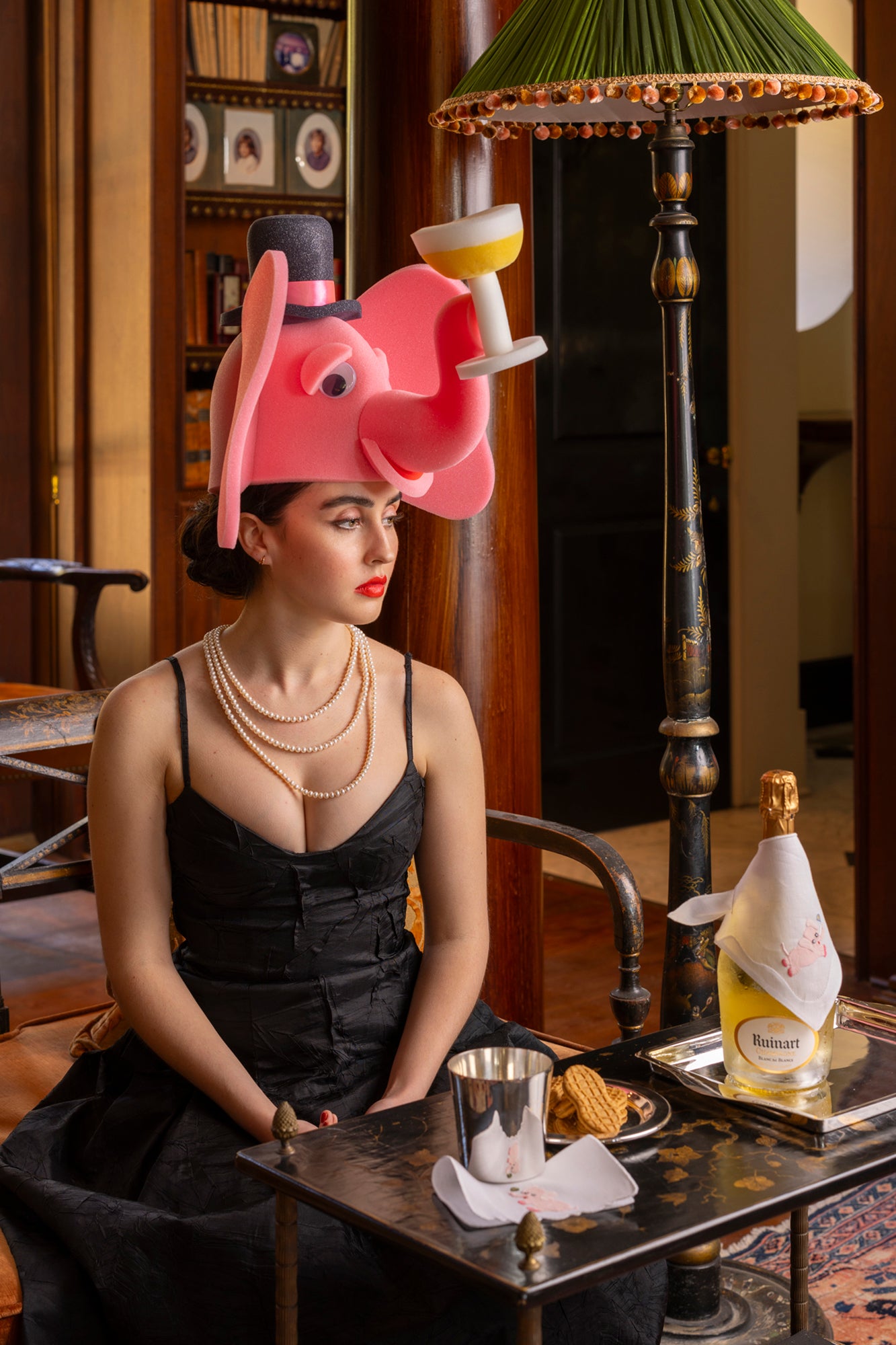 Girl in foam elephant hat in front of lamp with a shirred silk shade that is trimmed with tassel fringe from Paris.