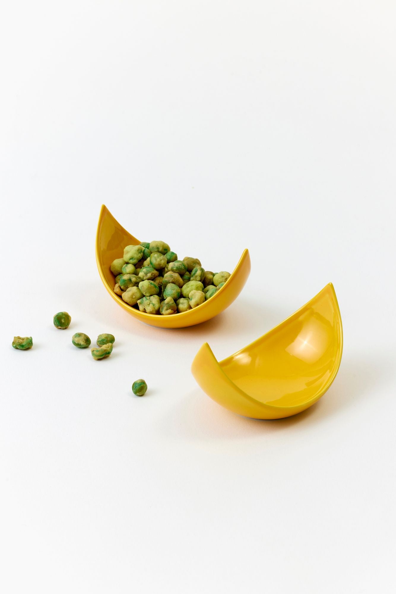 Yellow ceramic wedge dish with green wasabi peas on a white background