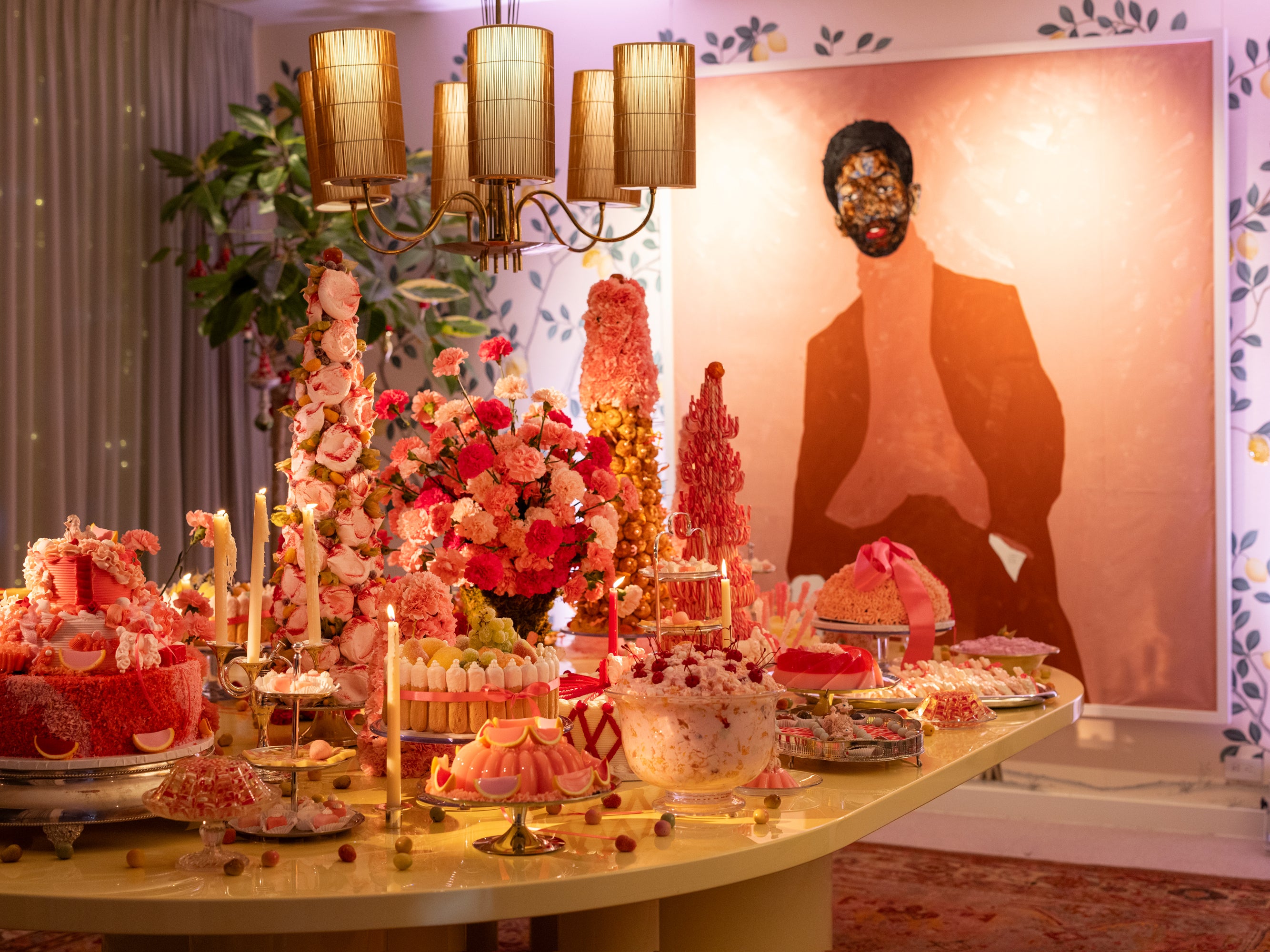 An abundant dessert table under rosy lighting set with colorful desserts, candles, and elegant pink florals.